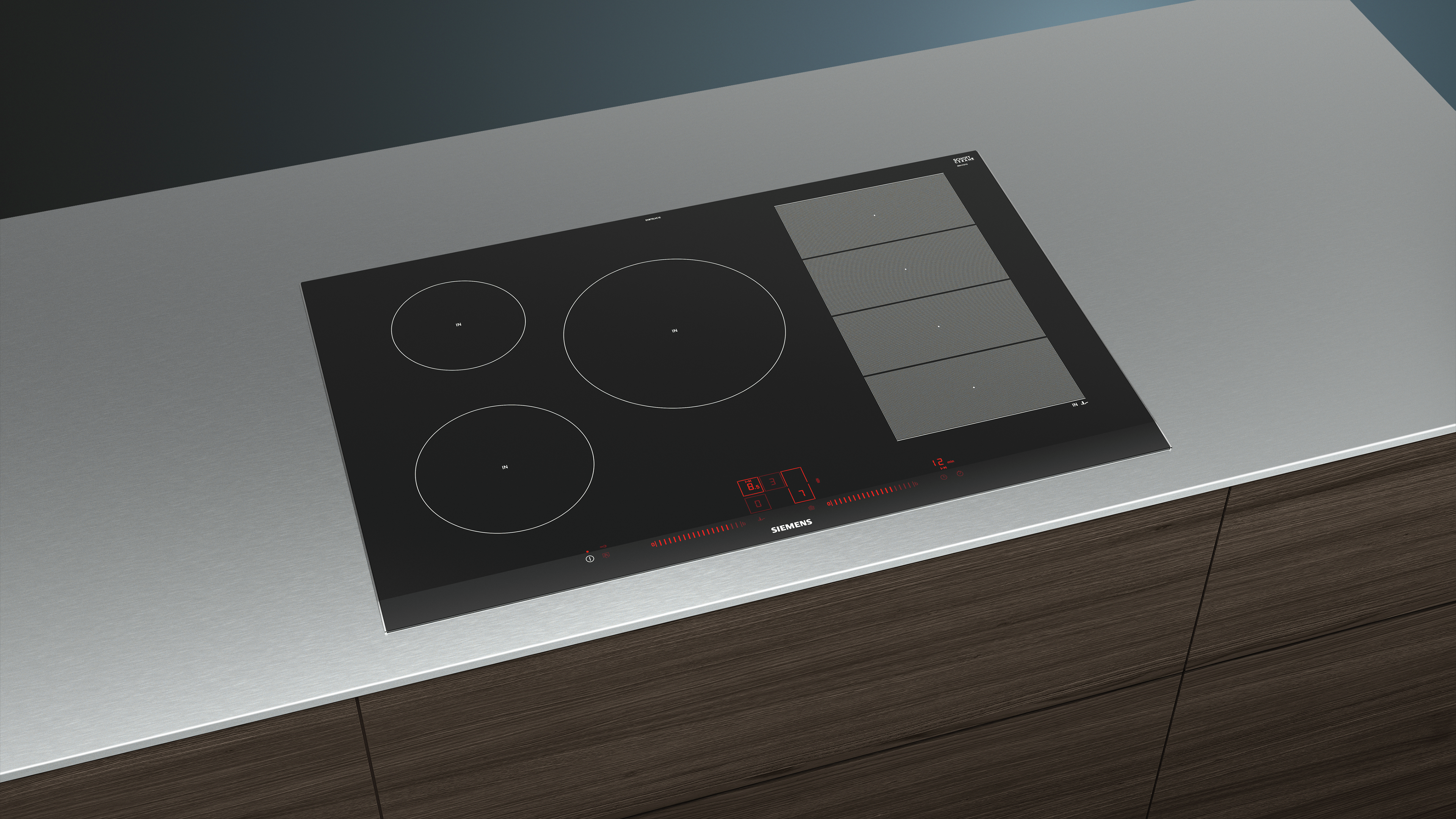 Table de cuisson à induction noire avec trois brûleurs et une hotte sur comptoir métallique.