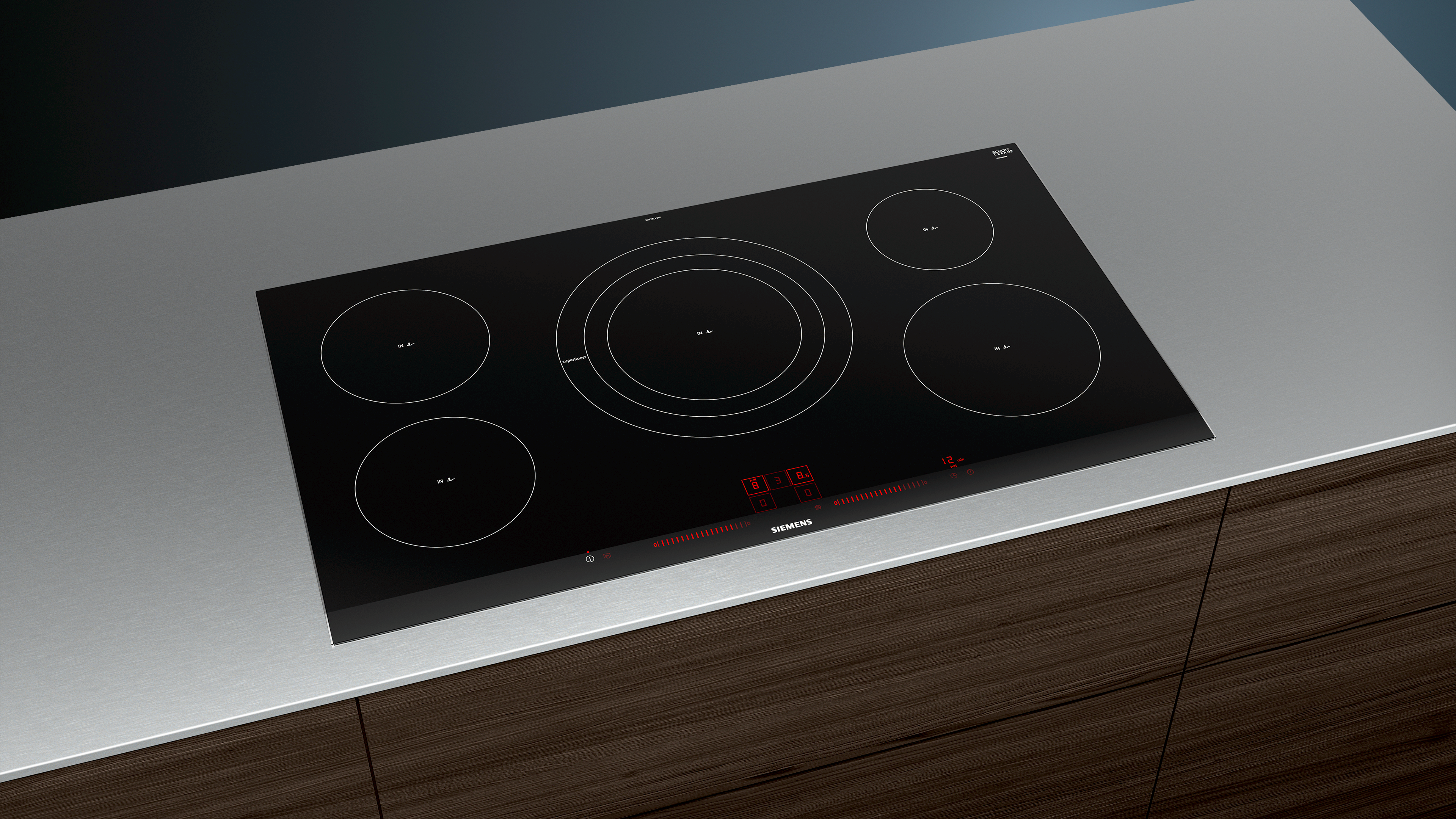 Table de cuisson à induction noire sur comptoir gris. Cinq zones de cuisson circulaires sont visibles.