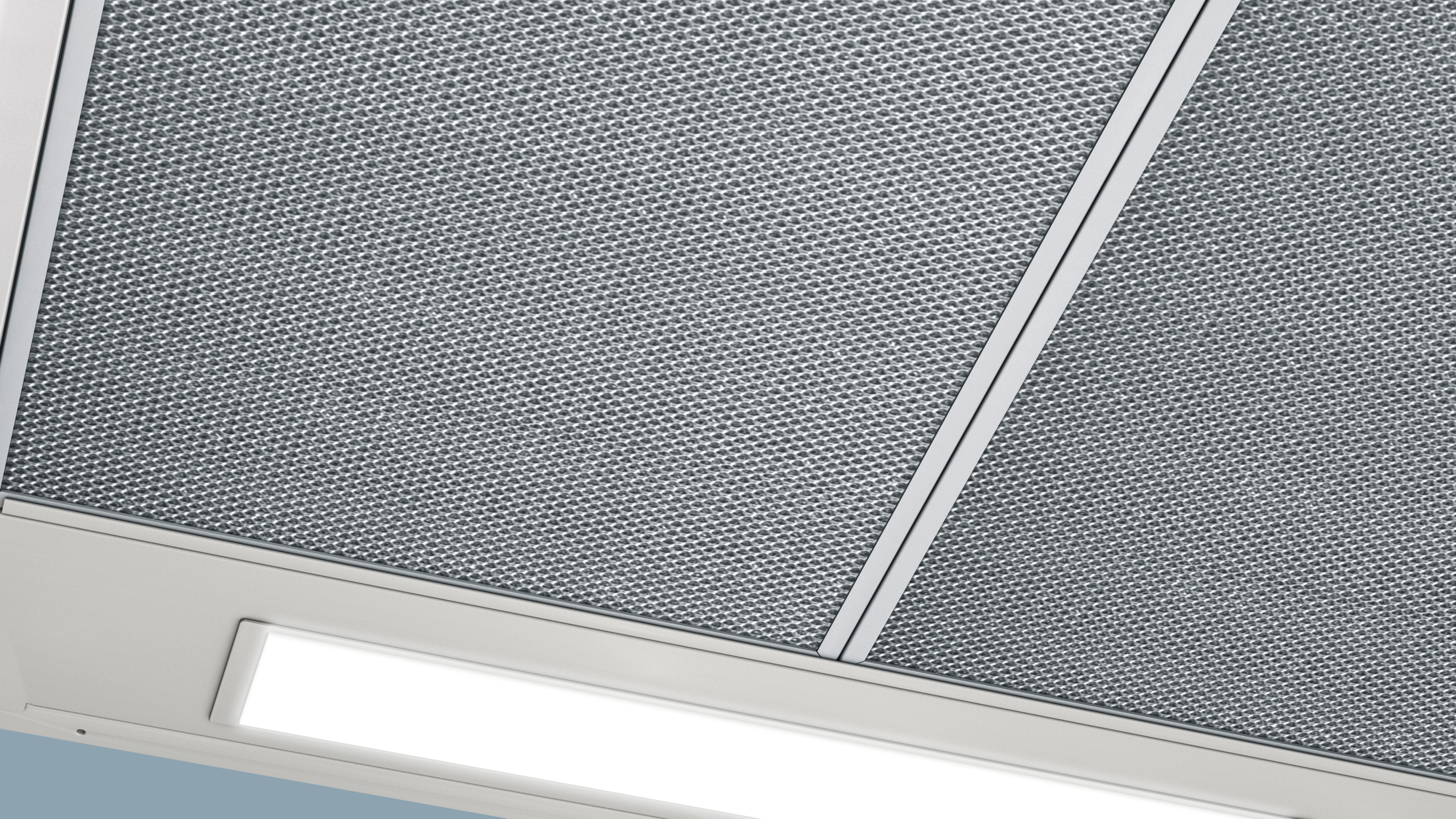 Close-up van een metalen gaasfilter in een witte afzuigkap met een licht.