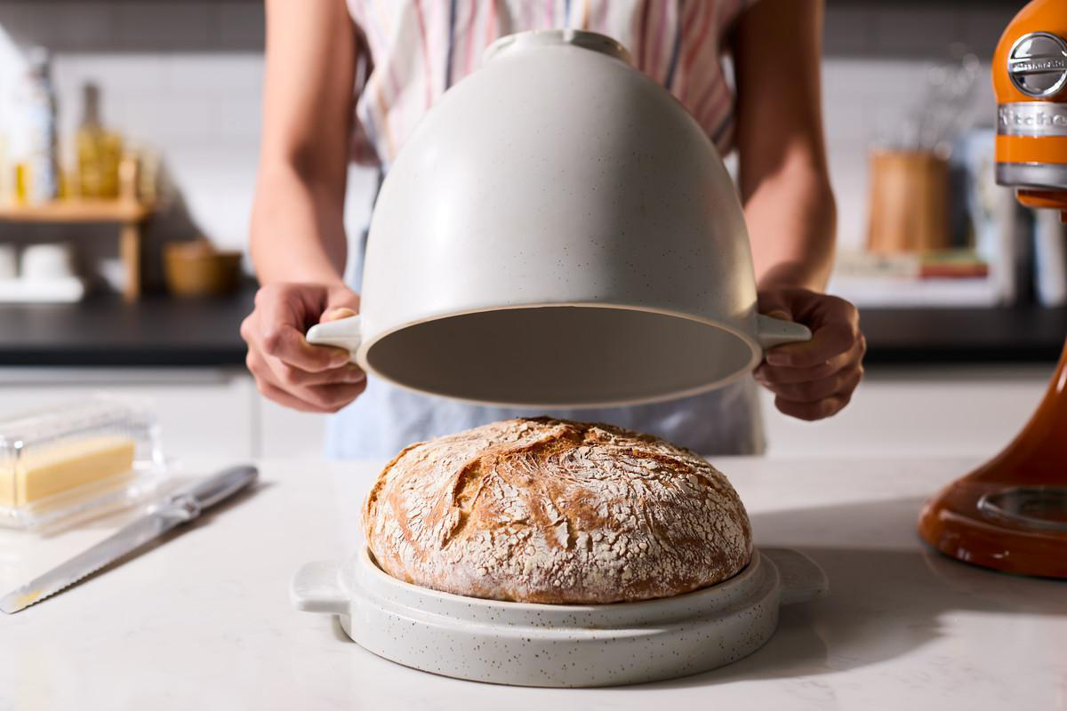 Eine Frau hält einen Deckel über einem Brotlaib in einem Keramik-Brotbackautomaten.