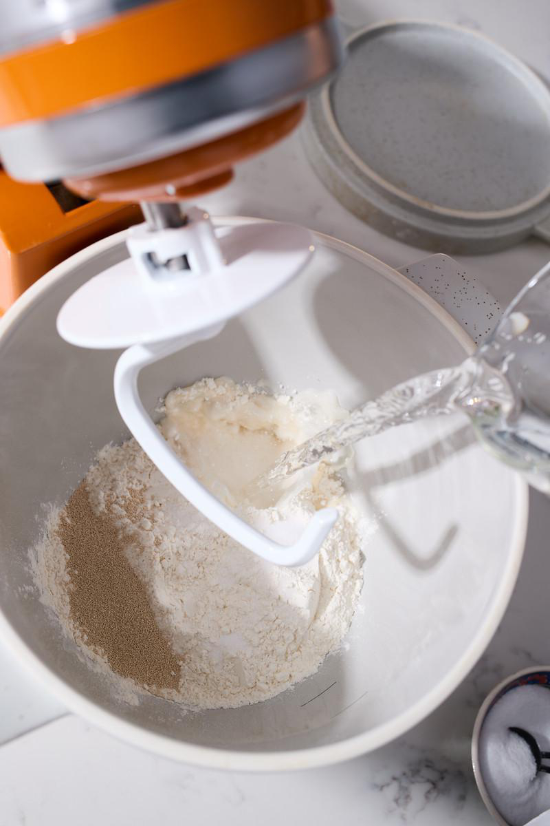 Wasser wird in eine Schüssel mit Mehl und Hefe gegossen.