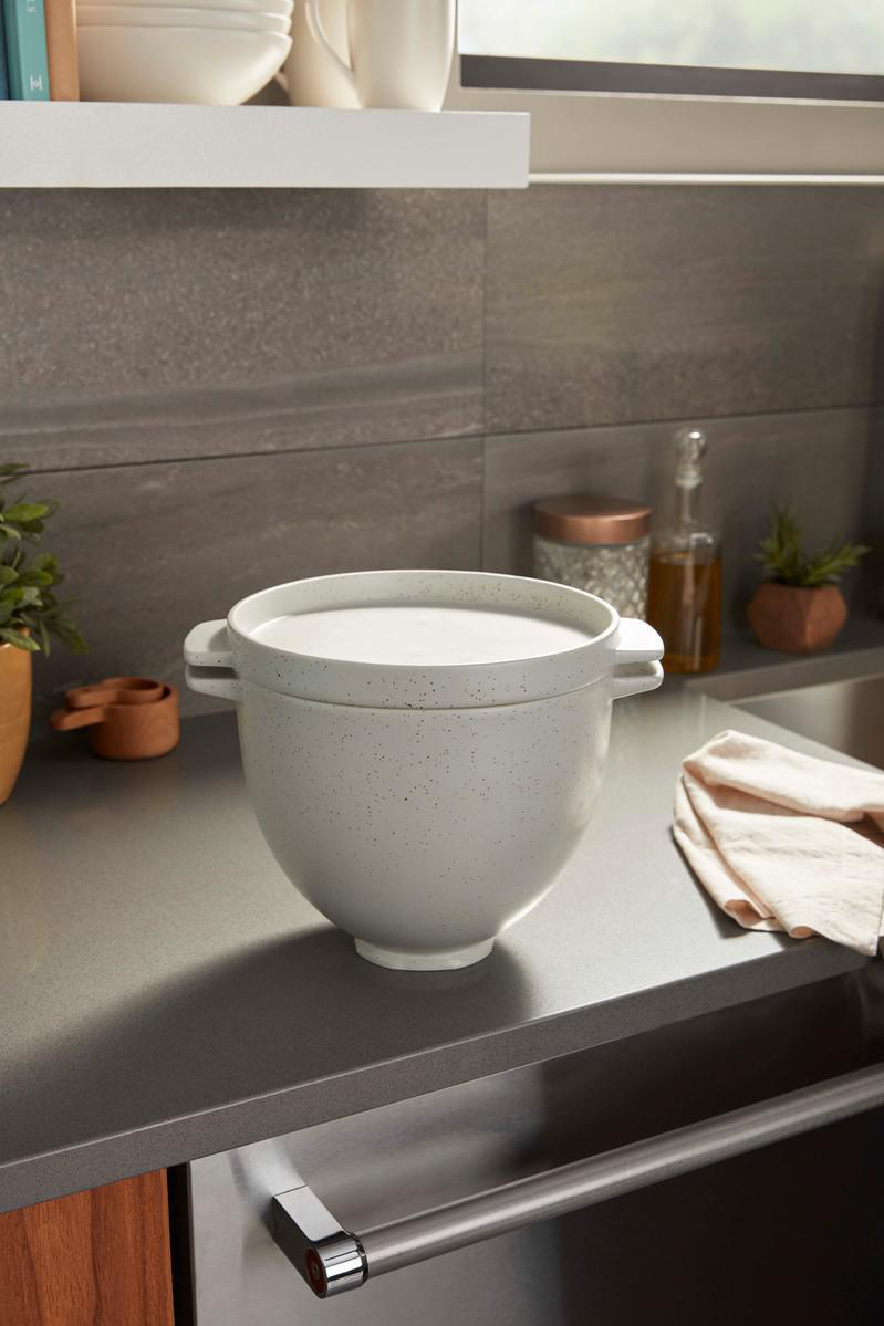 Weiße Küchenmixer-Schüssel auf einer Theke. Graue Arbeitsplatte, neutraler Hintergrund.