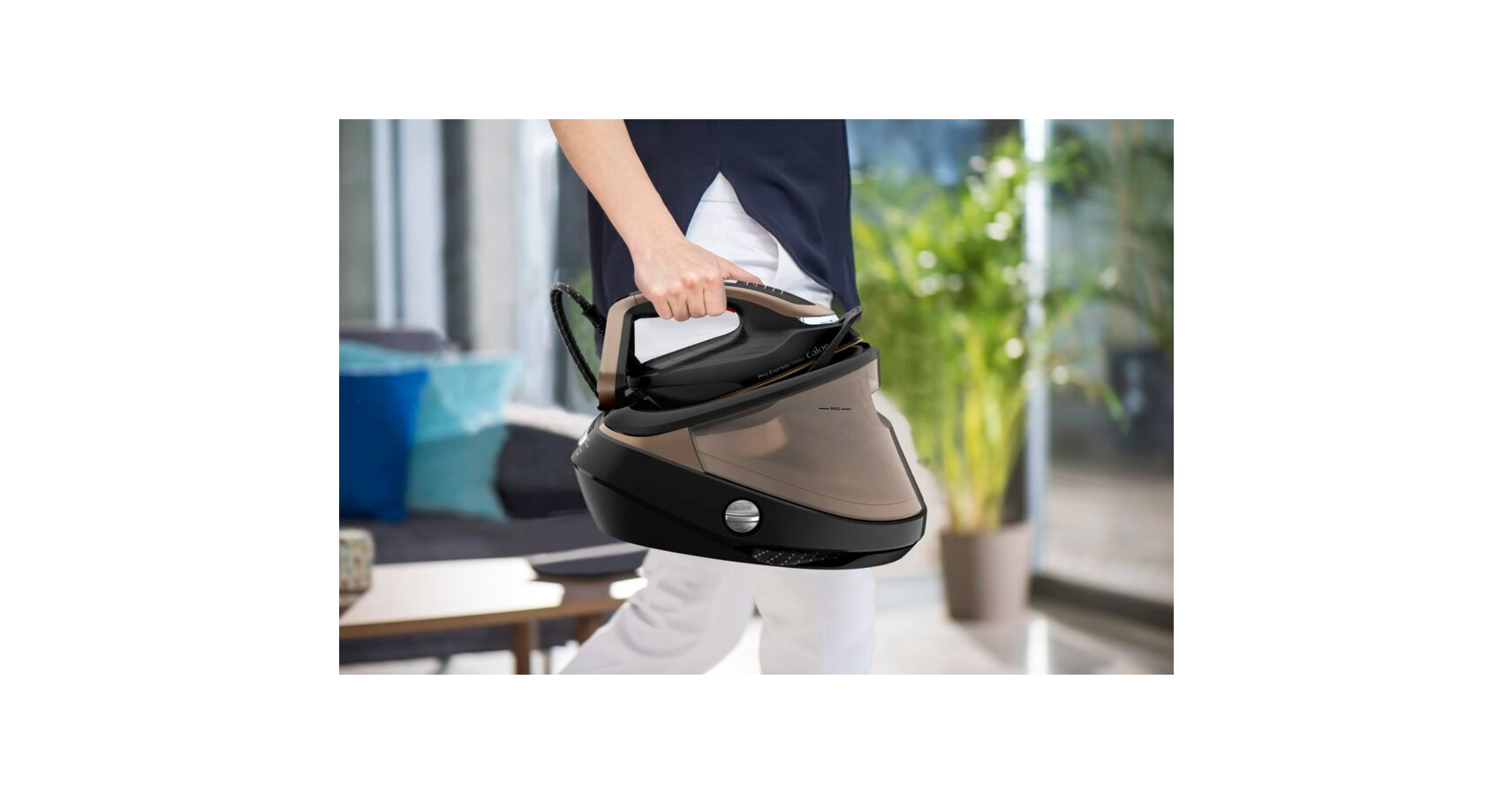 A person holding a black and tan steam iron, in a room.