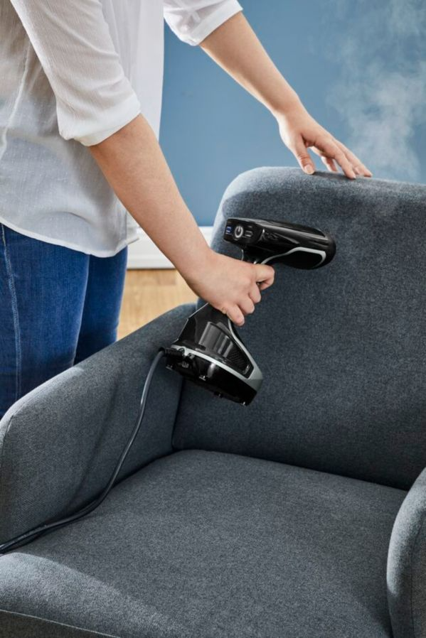 A person steaming a grey armchair with a black and grey steamer.