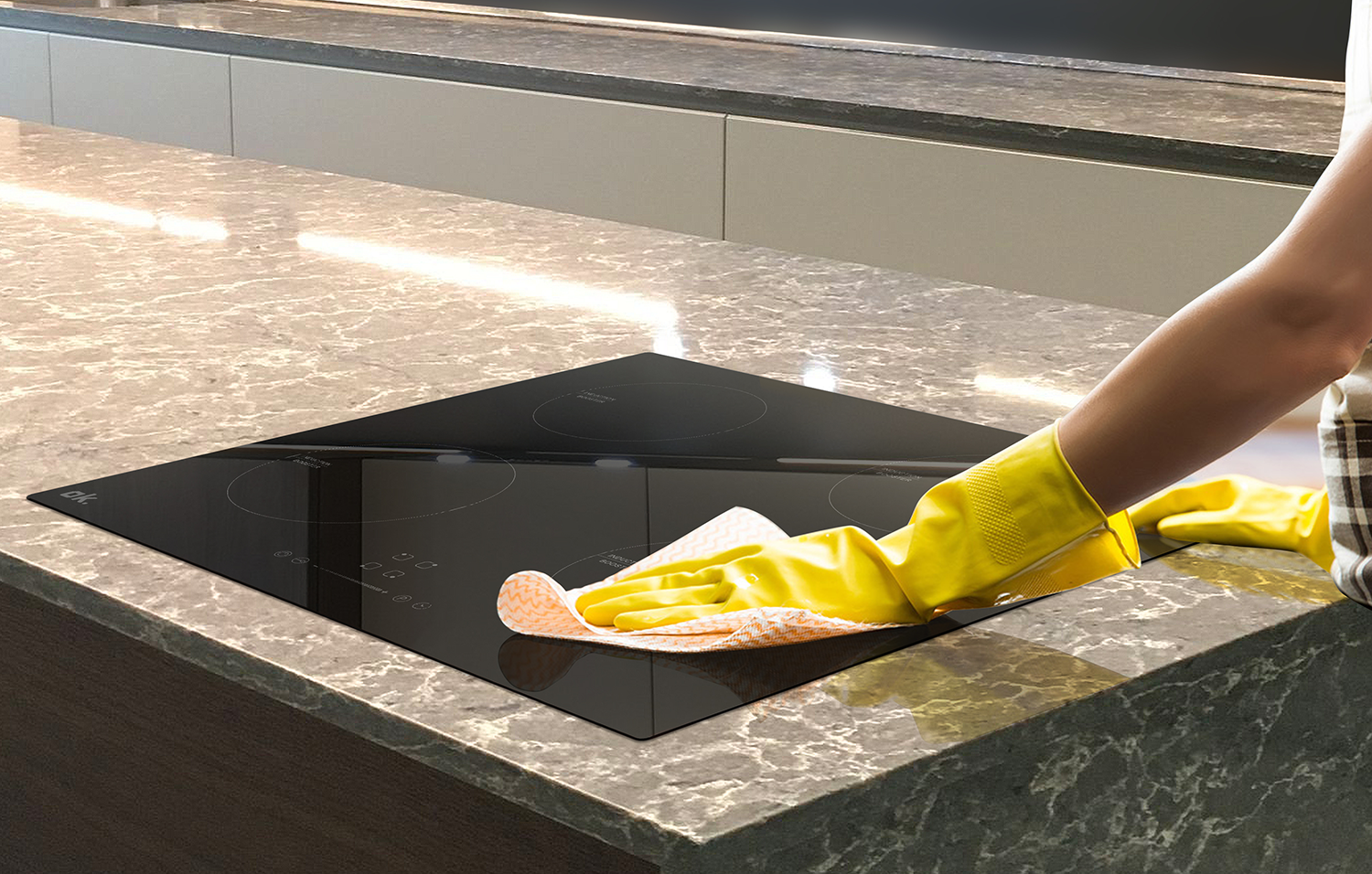 Person wiping a black induction cooktop with a cloth and yellow gloves.