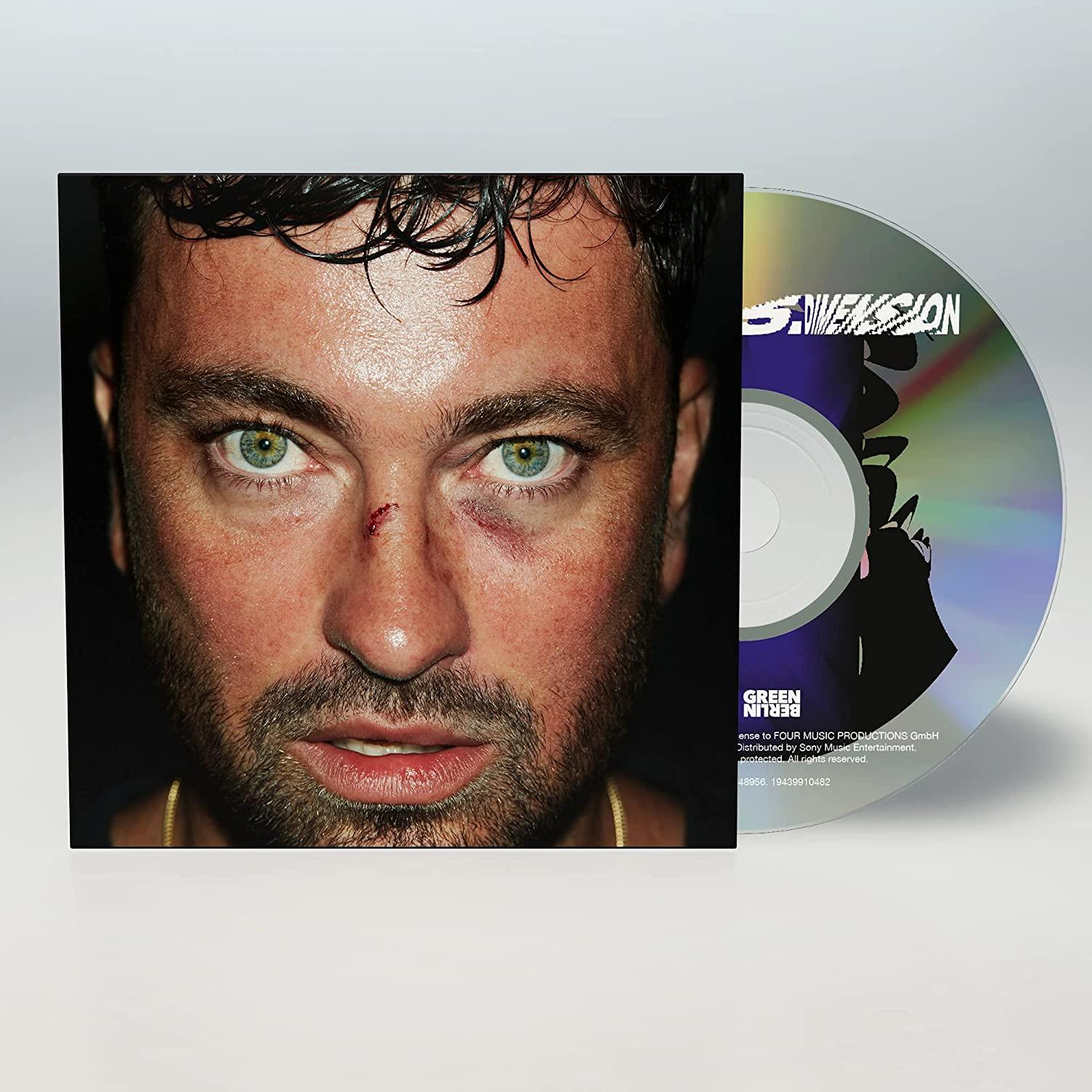 Nahaufnahme eines Mannes mit blauem Auge, einer CD und einer CD-Hülle mit Text und Logo.