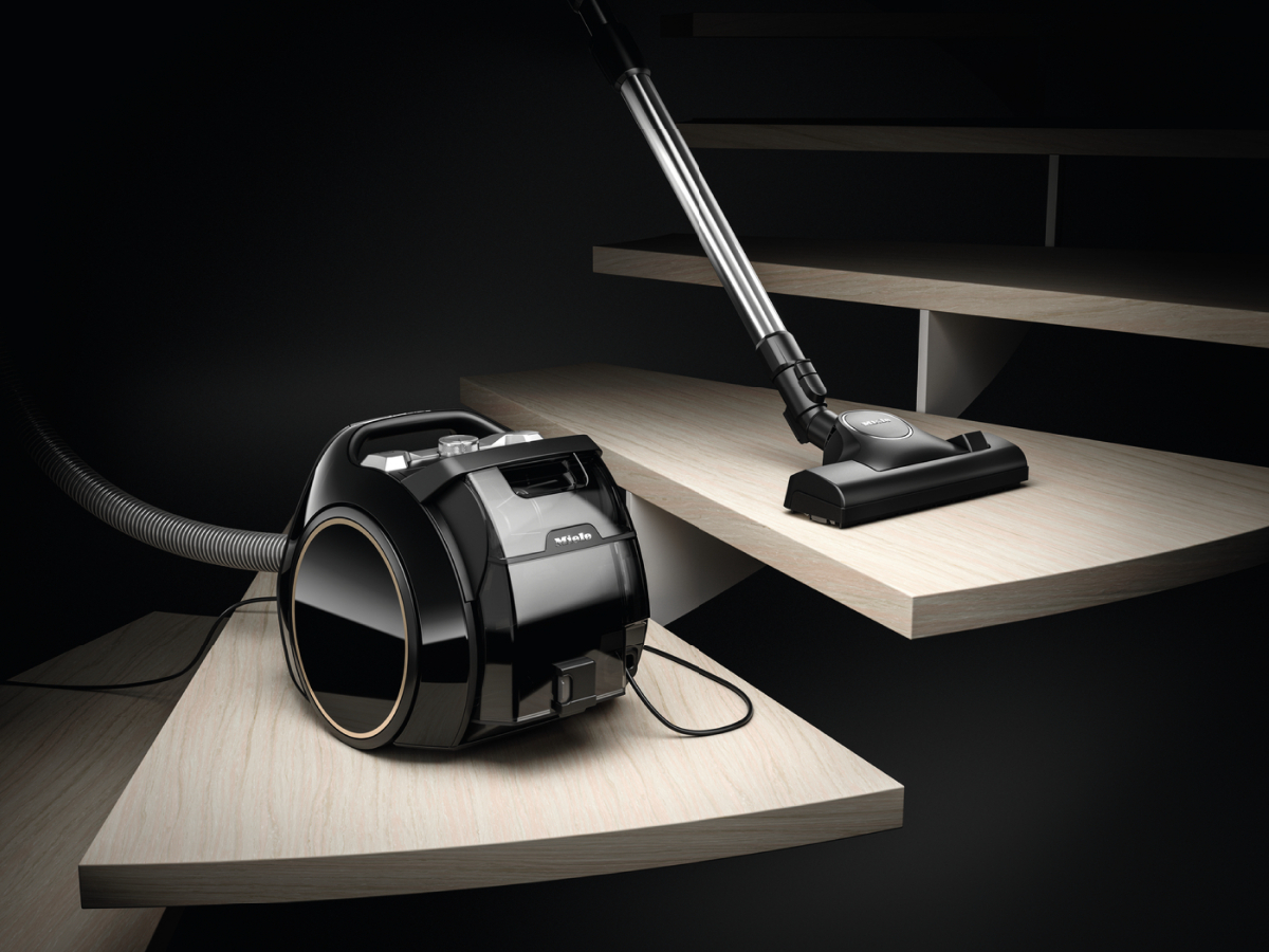 Black vacuum cleaner on wooden stairs. A vacuum cleaner is on the floor, another is on the stairs.