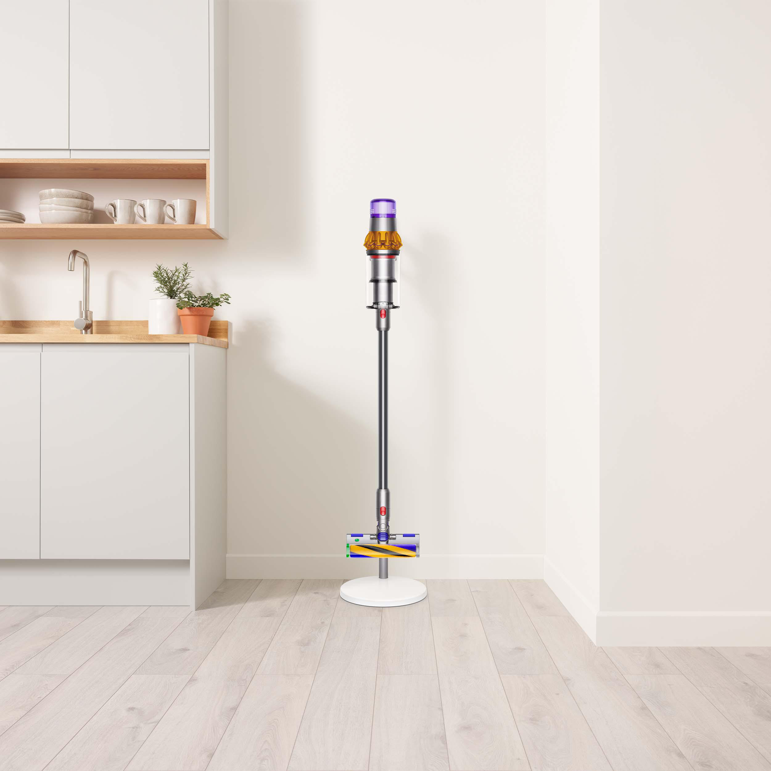 Ein moderner Staubsauger steht aufrecht in einer Küche, neben einer weißen Wand und Holzboden.