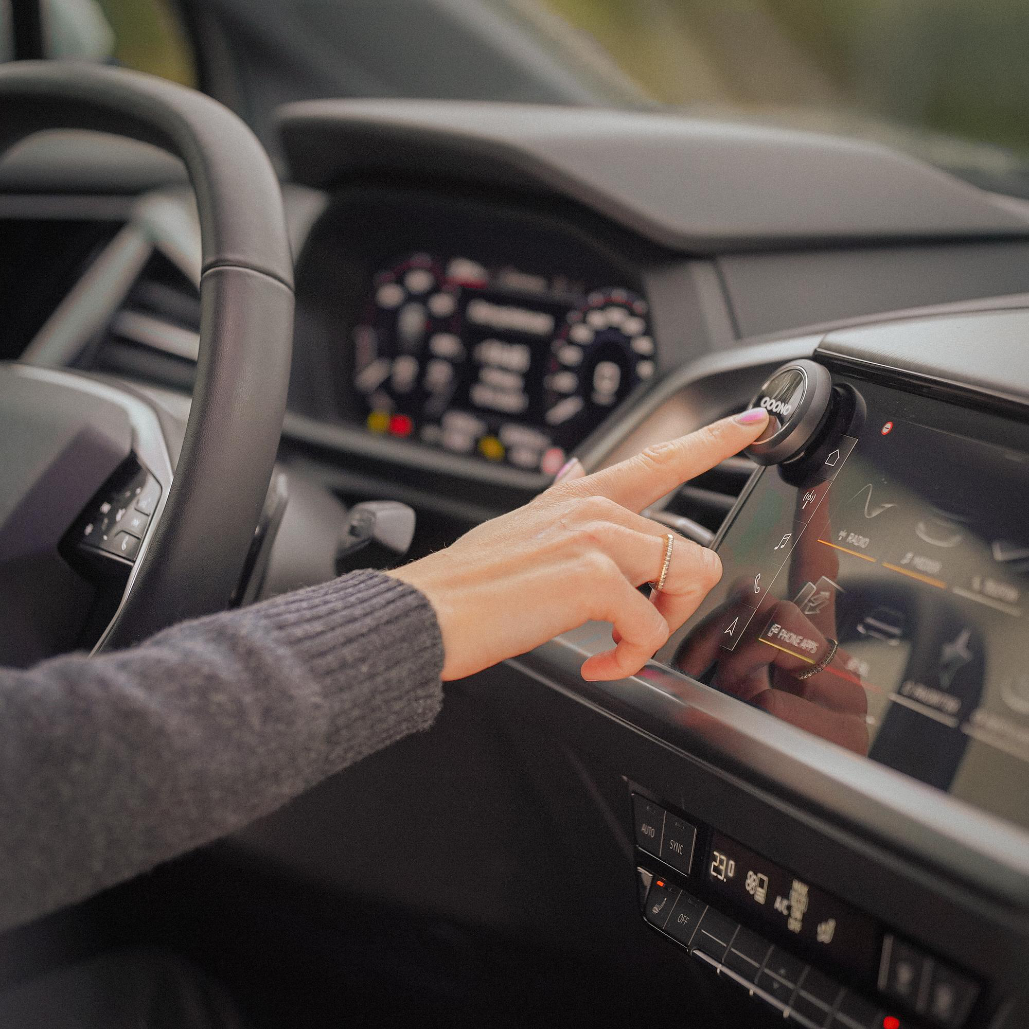 Eine Hand berührt ein schwarzes kreisförmiges Gerät in einem Auto. Das Gerät ist am Armaturenbrett montiert.