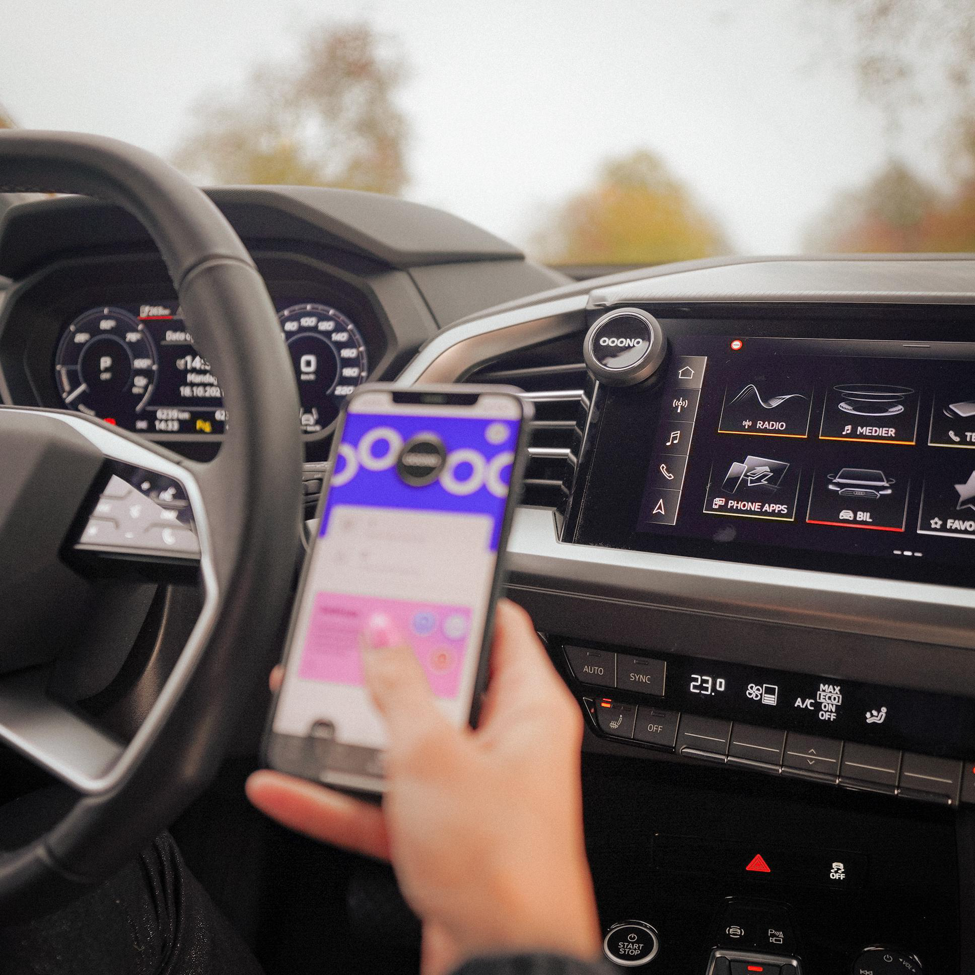 Person im Auto benutzt Handy mit App. Armaturenbrett und Lenkrad sichtbar.