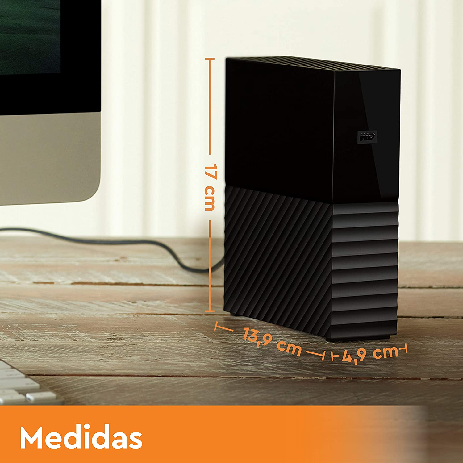 Un disco duro externo negro sobre una mesa de madera. Las medidas se muestran en naranja.