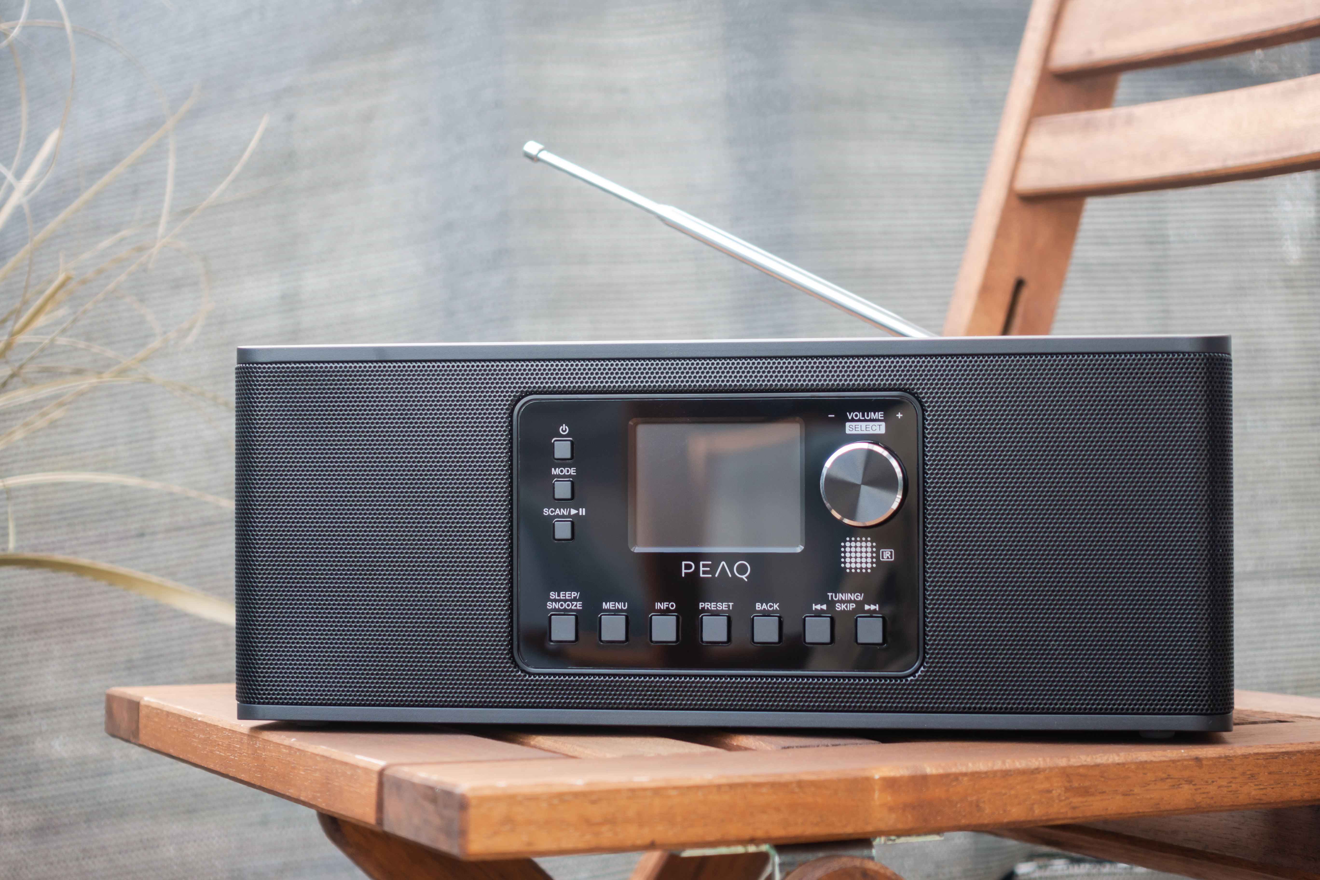 Schwarzes Radio mit Bildschirm auf einem Holzstuhl im Freien.