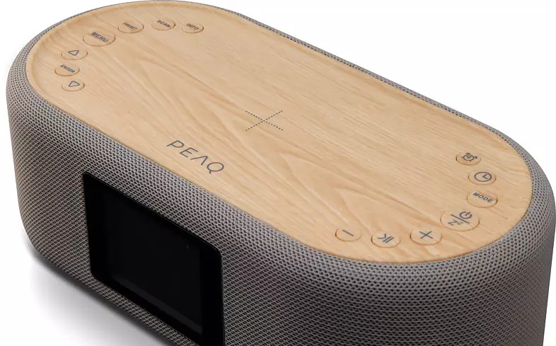 Haut-parleur ovale en bois avec une enveloppe en tissu. Il a des boutons sur le dessus et un petit écran.