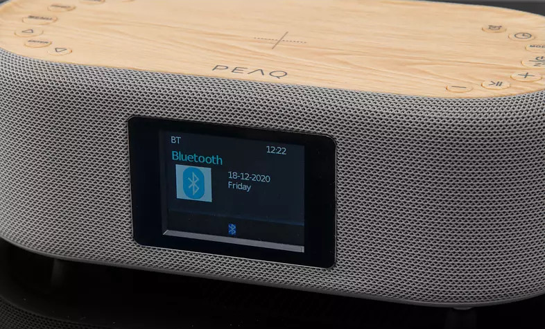 Un haut-parleur PEAQ avec un écran affichant la connexion Bluetooth et la date, sur fond sombre.