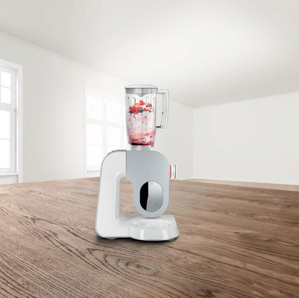 Mixer mit einem durchsichtigen Krug, der mit Früchten gefüllt ist. Der Mixer steht auf einem Holztisch.