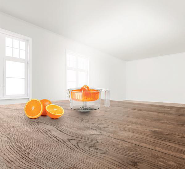 Eine Saftpresse mit Orangen auf einem Holztisch in einem weißen Raum. Eine Orange ist halbiert.