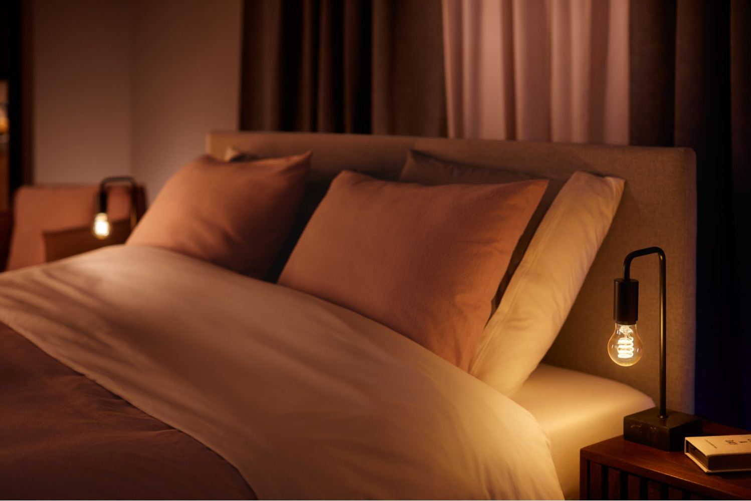 Scène de chambre à coucher avec lit, oreillers et une lampe de chevet avec une ampoule allumée.