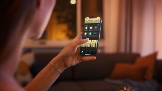 Personne tenant un smartphone, affichant une application domotique. Commandes d'éclairage visibles.