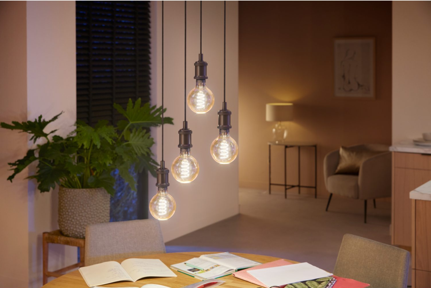 Quatre ampoules de style Edison sont suspendues au-dessus d'une table à manger. Une plante et une peinture sont également dans la scène.