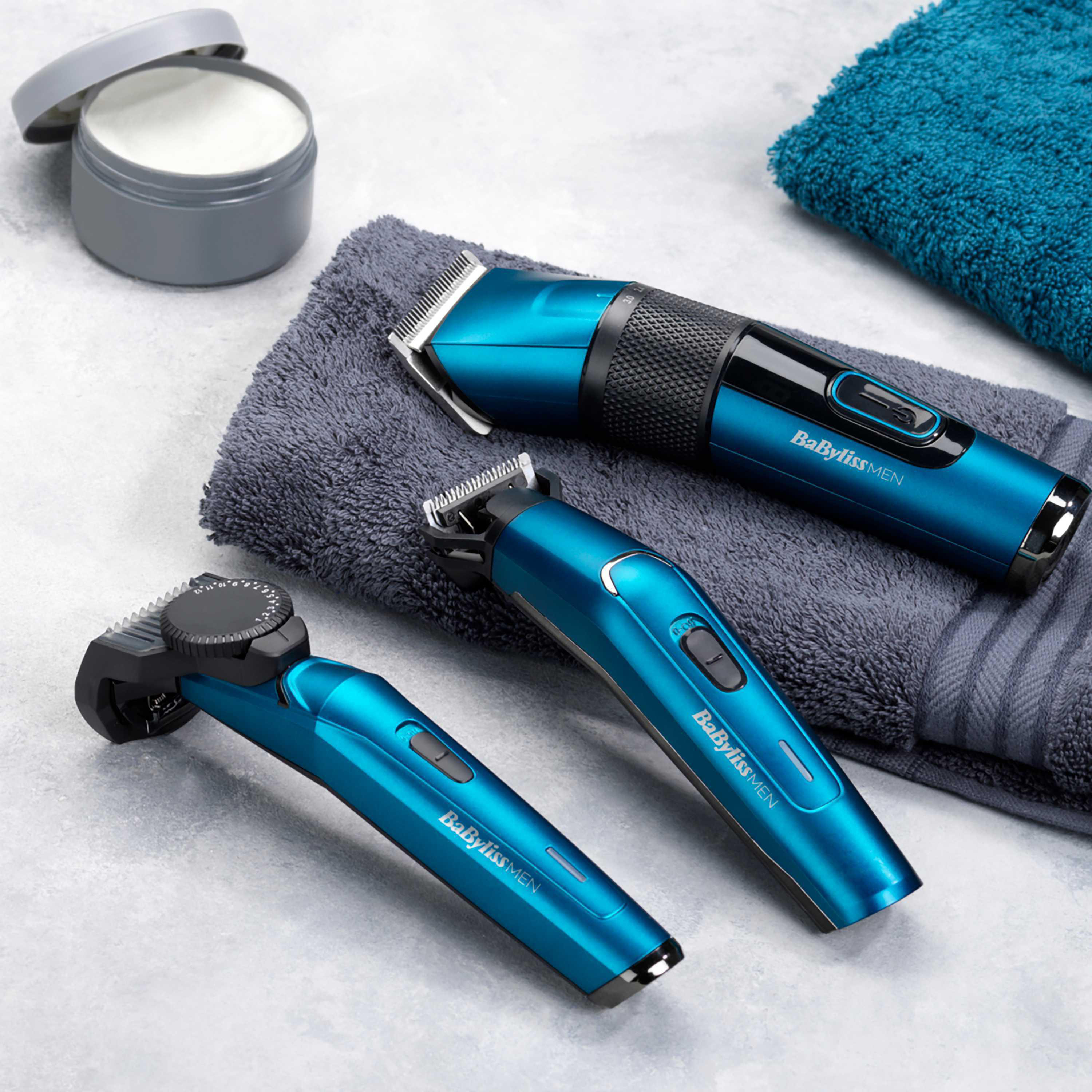 Drei blaue und schwarze elektrische Bartschneider und Pflegezubehör auf einem Handtuch.