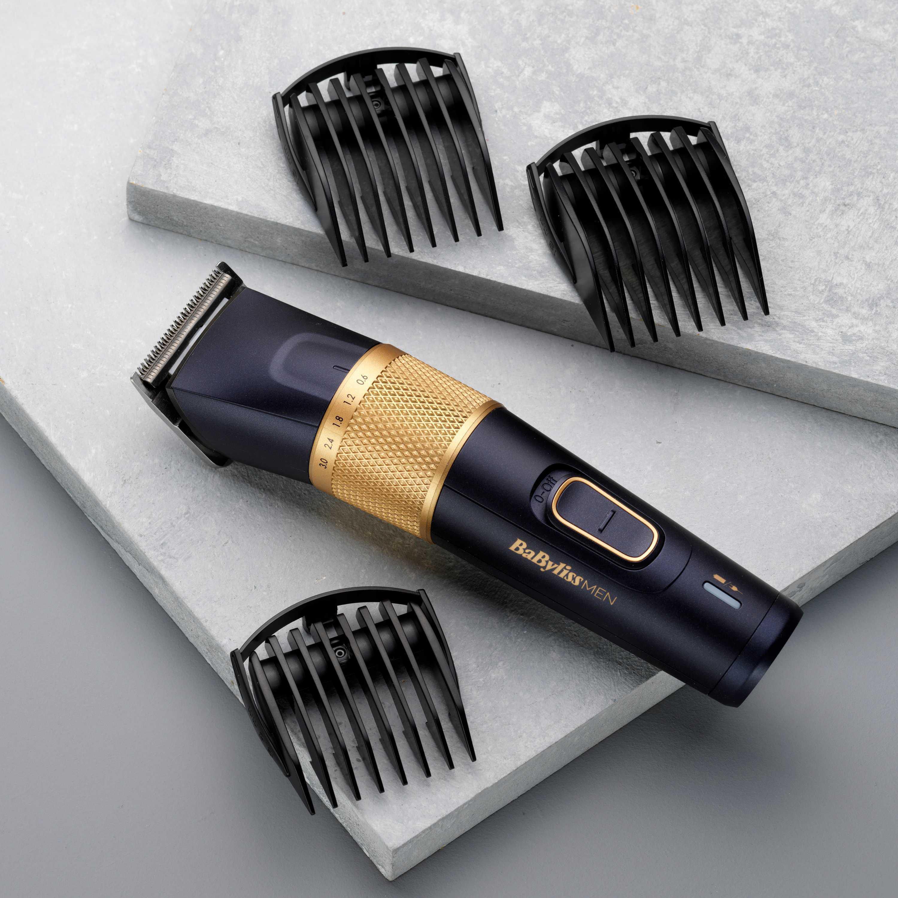 Ein schwarz-goldener Haarschneider mit drei schwarzen Kammaufsätzen auf grauer Oberfläche.