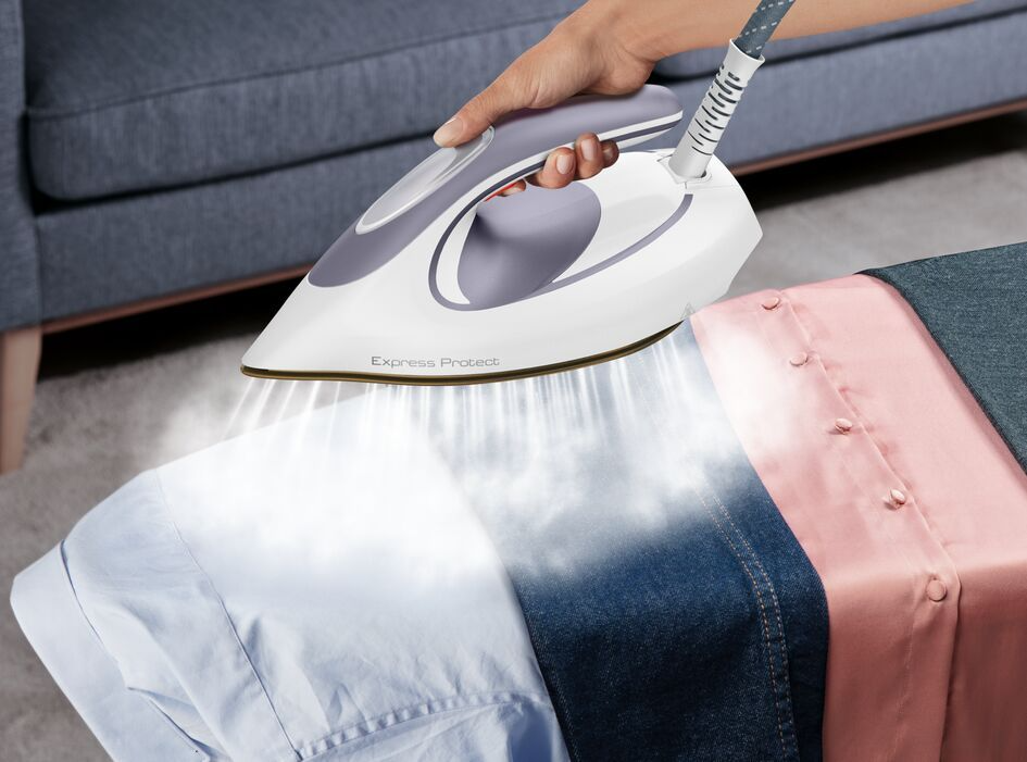 A person ironing shirts with a white and grey iron, steam rising, shirts on the right.