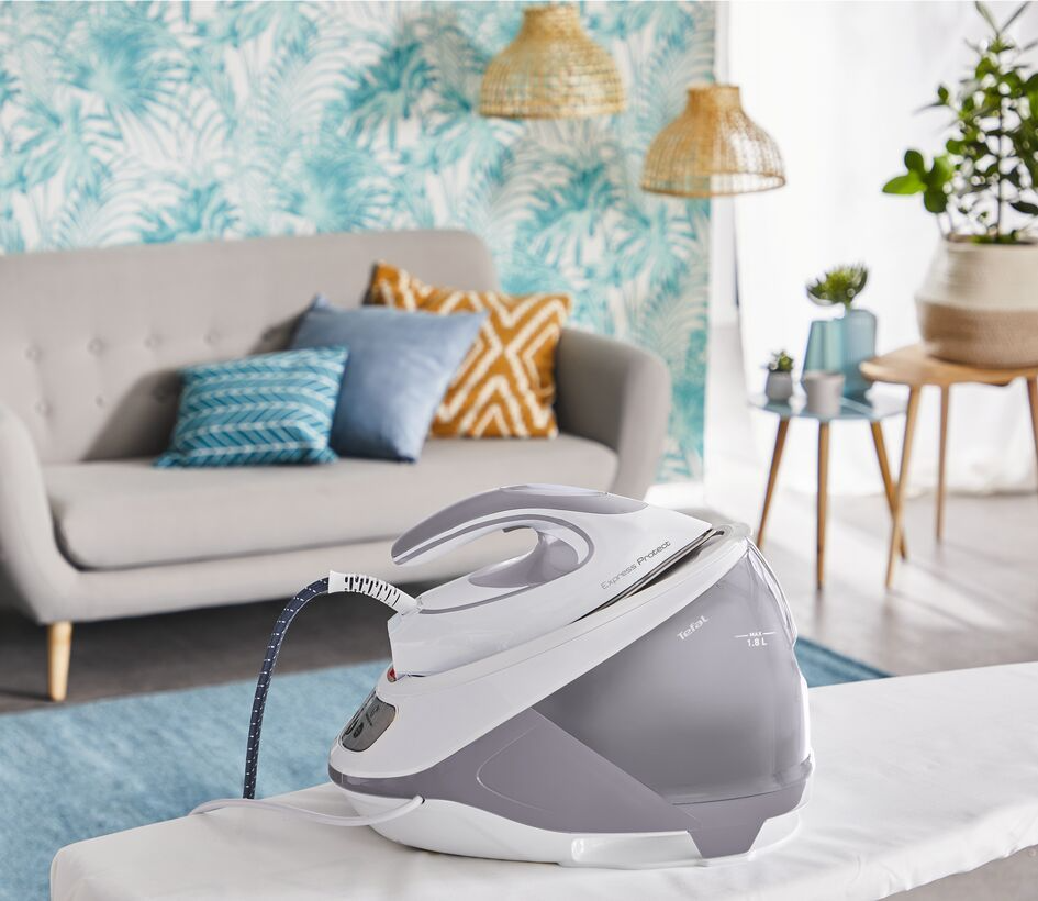 An iron on an ironing board, with a water tank, in front of a sofa and decor.