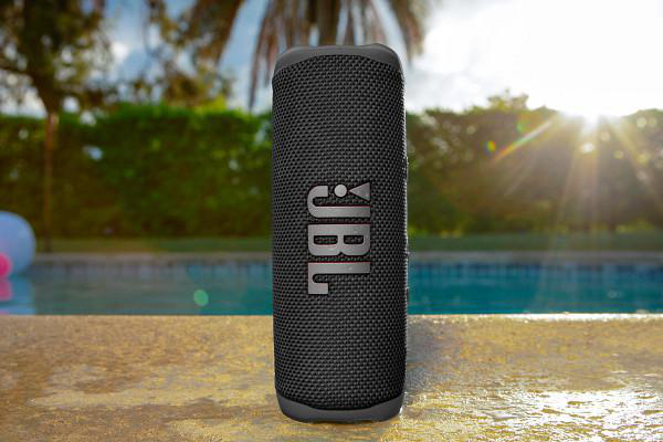 Schwarzer JBL-Lautsprecher an einem Pool mit Bäumen und Sonnenlicht im Hintergrund.