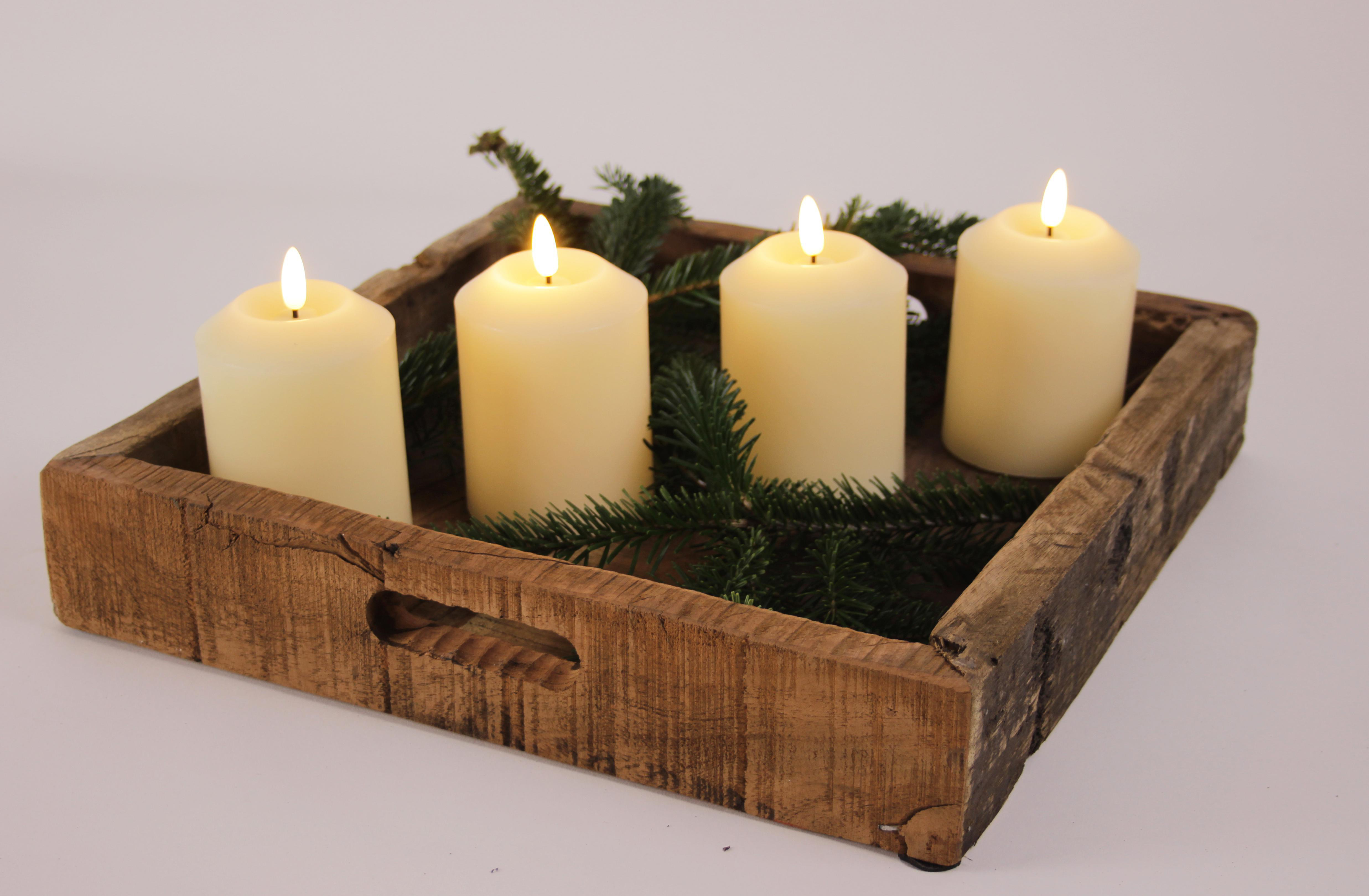 Ein Holztablett mit vier brennenden Kerzen und grünen Tannenzweigen. Weißer Hintergrund.