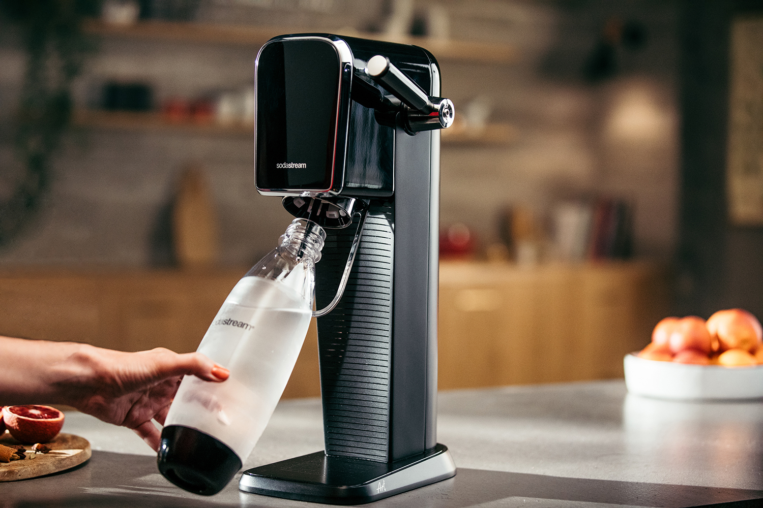 Zwarte SodaStream machine met een fles die gevuld wordt. Keukenomgeving.