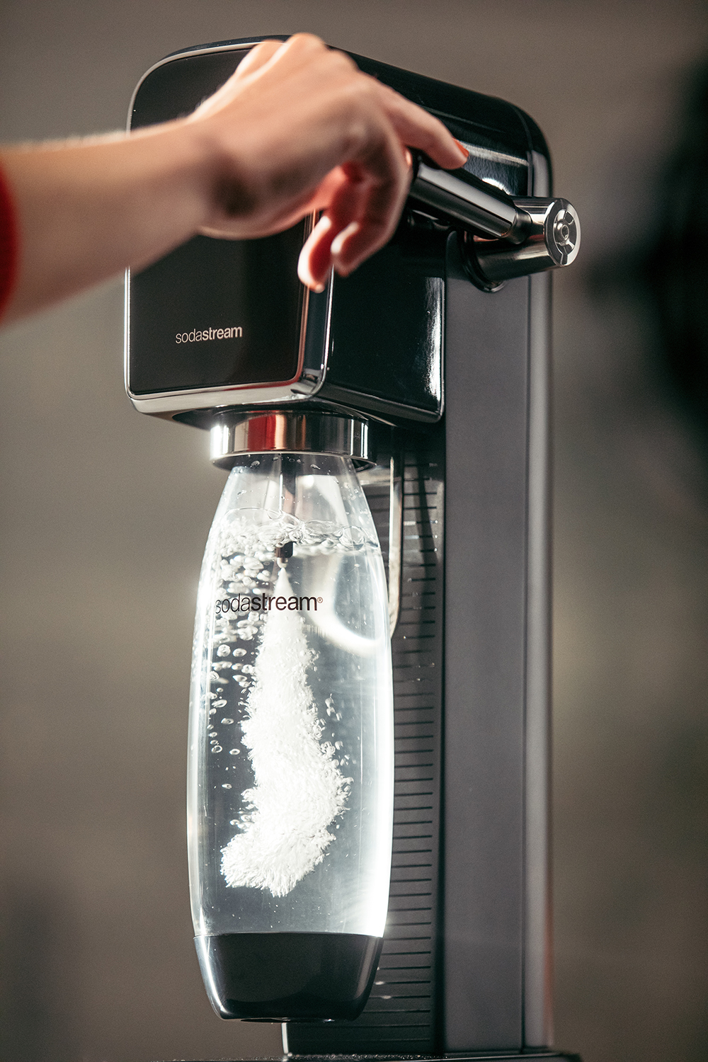 Een persoon die een SodaStream gebruikt. Een fles vult zich met bellen. De achtergrond is wazig.