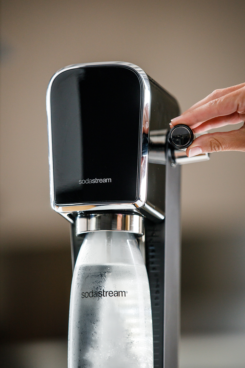 Een zwarte SodaStream met een fles. Een hand draait aan een knop bovenop de SodaStream.