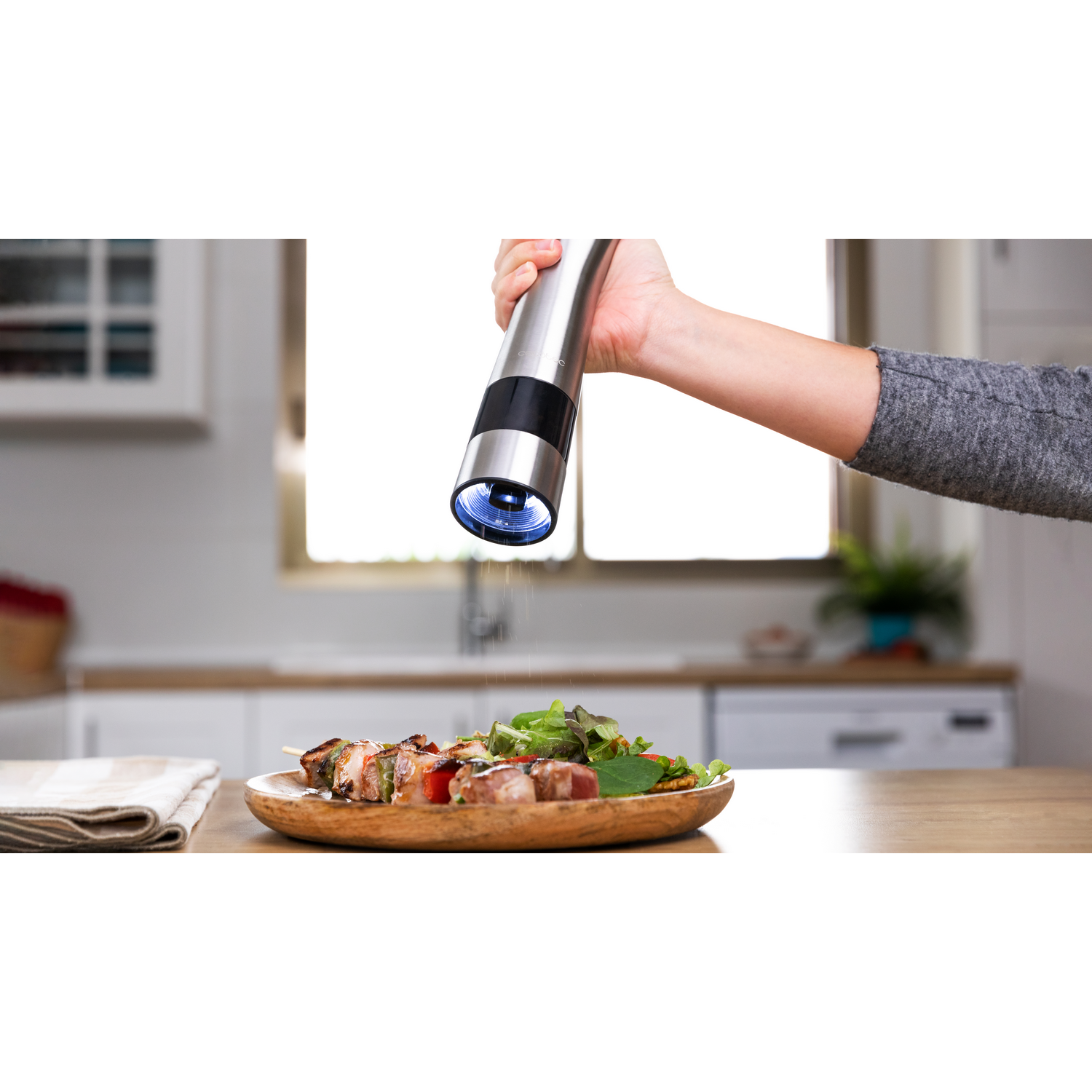 Una persona moliendo sal sobre un plato de comida con un molinillo eléctrico plateado.