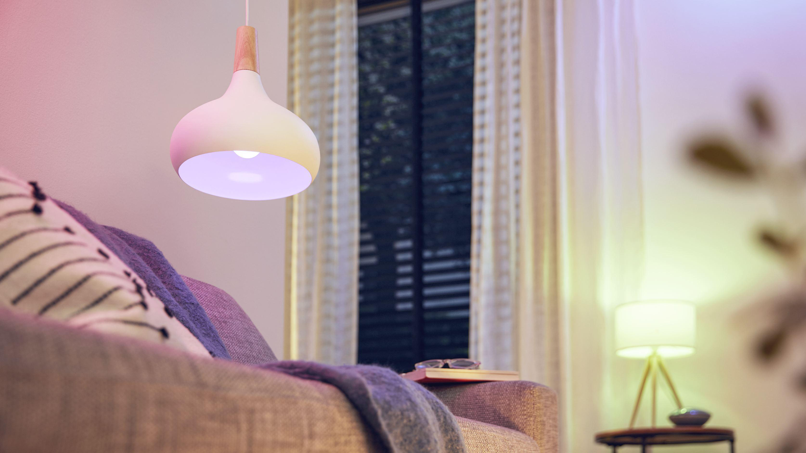 Eine weiße und hölzerne Lampe hängt über einem Sofa und Büchern in einem Raum mit Fenster.