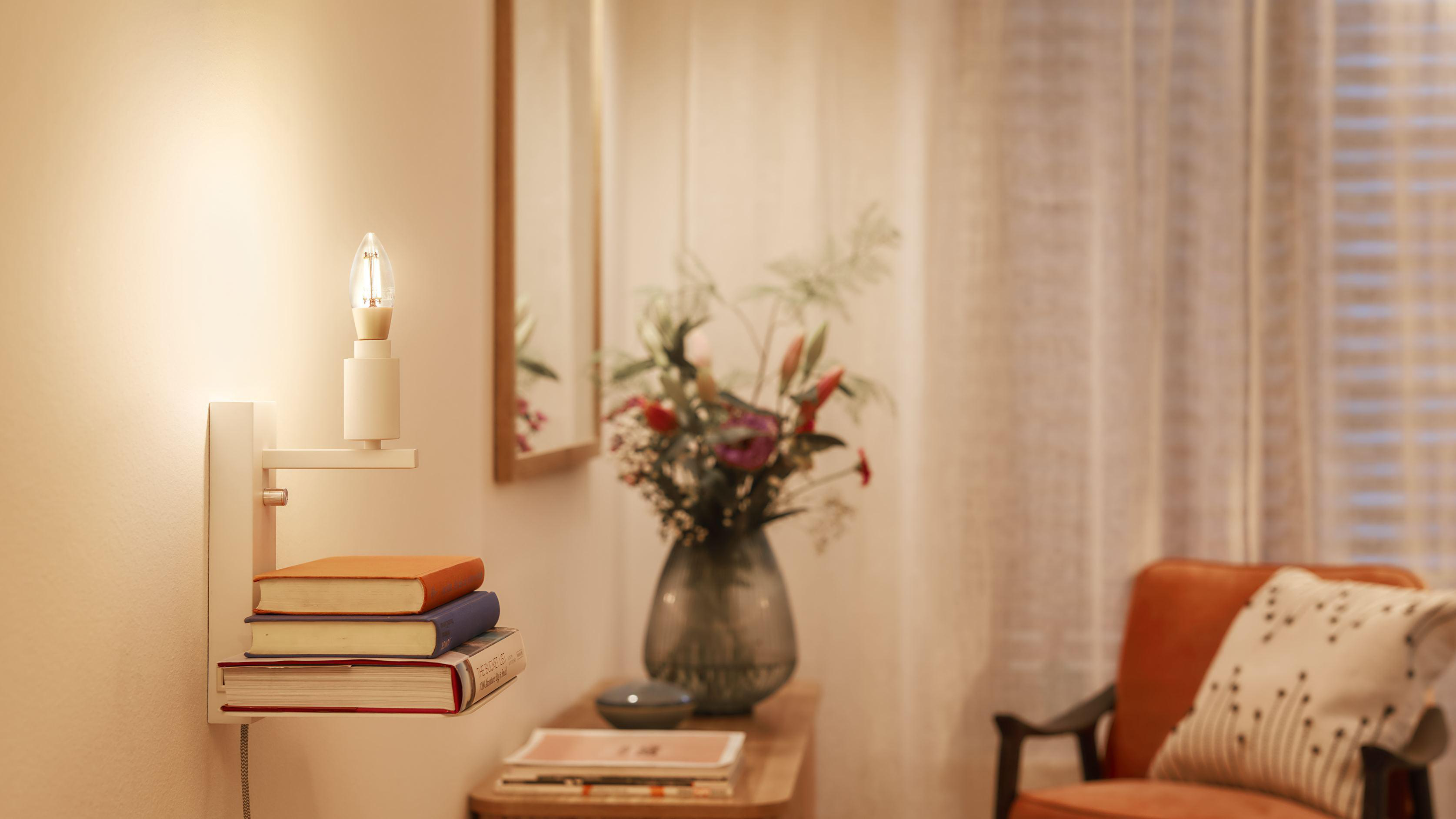 Eine Wand mit Lampe, Büchern und Blumen. Warmes Licht füllt die Szene.