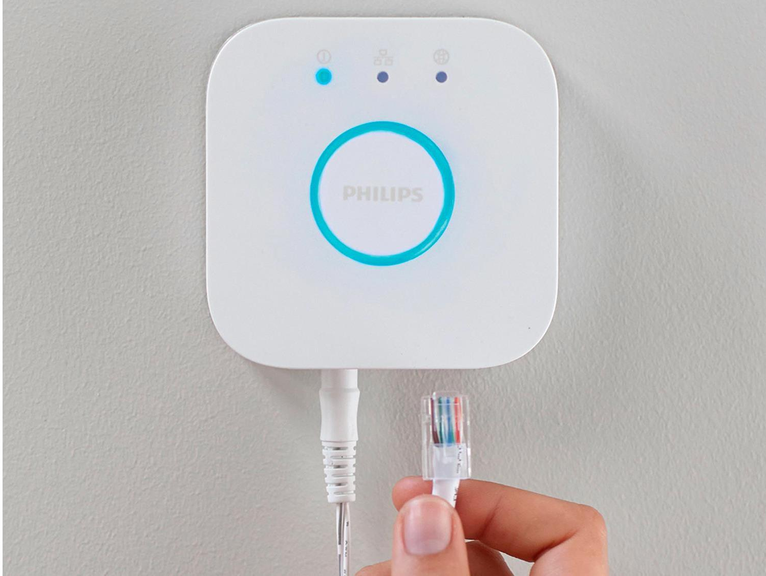 Appareil Philips Hue Bridge blanc avec une main tenant le câble réseau. Lumières bleues et vertes.