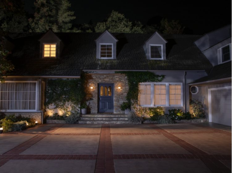 Vue nocturne d'une maison avec lumières allumées, allée en briques.