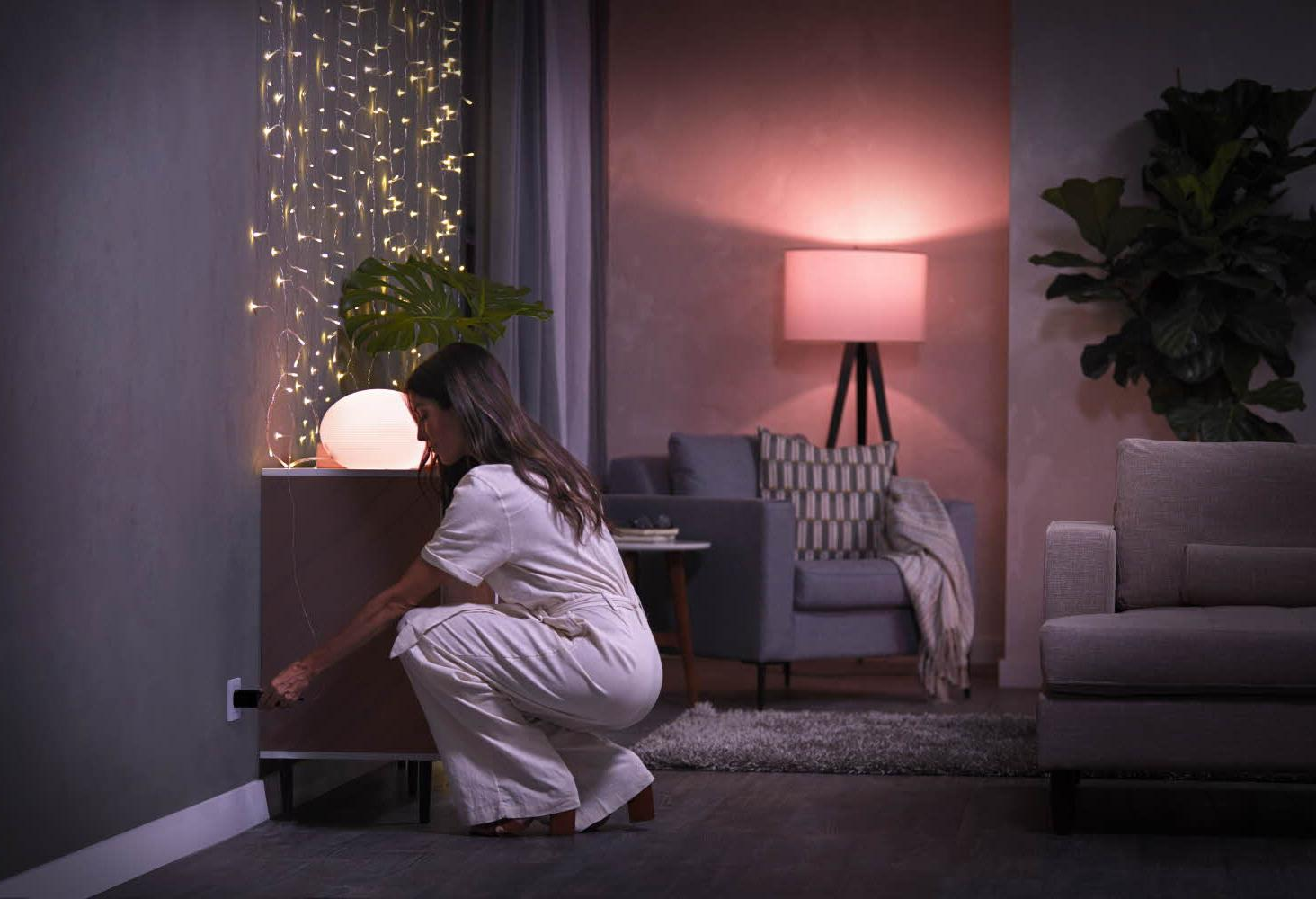 Une femme branchant une lampe dans une prise murale, dans une pièce avec une lampe et un canapé.