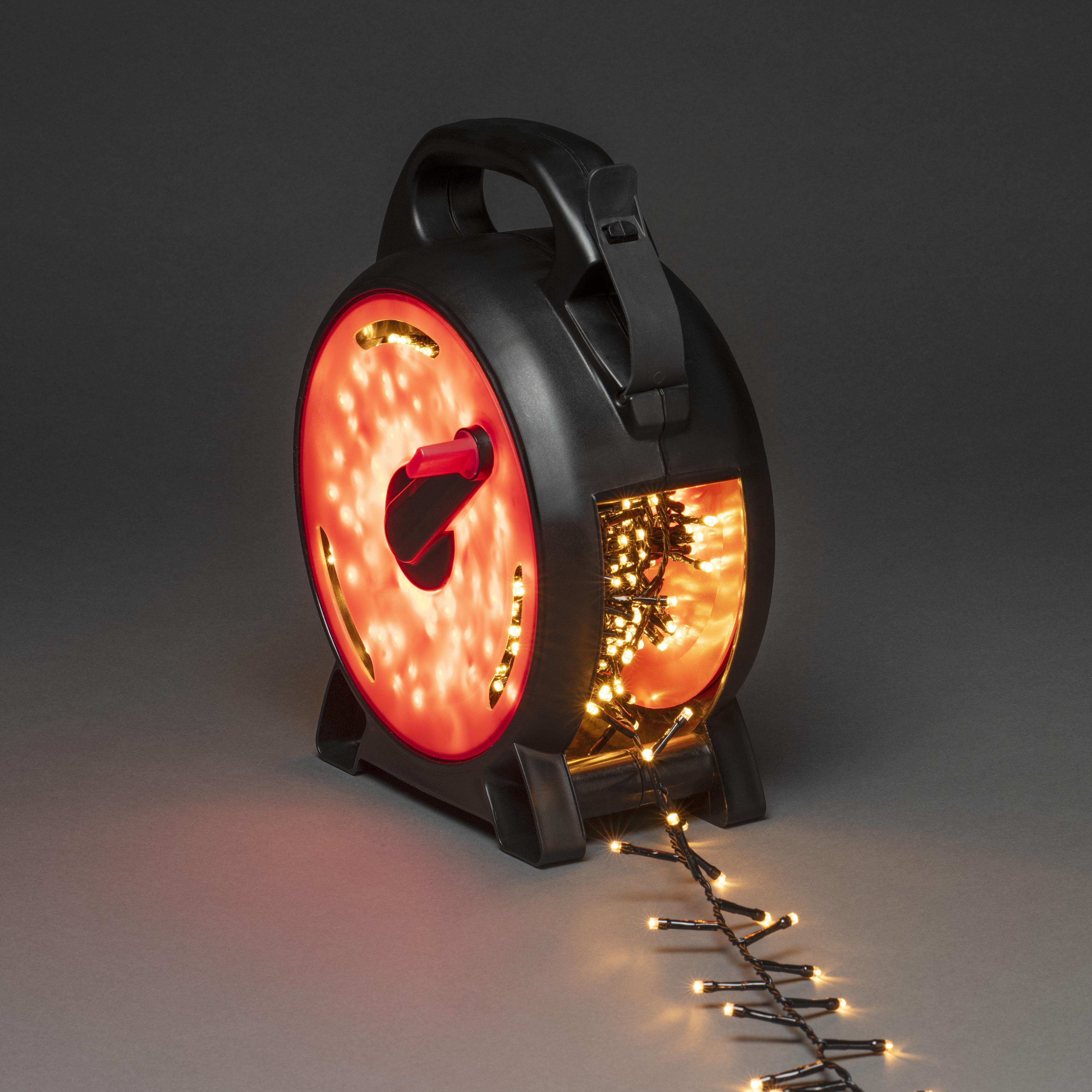 Schwarze Rolle mit Weihnachtsbeleuchtung. Lichter sind an. Rotes Licht scheint durch die Rolle. Grauer Hintergrund.