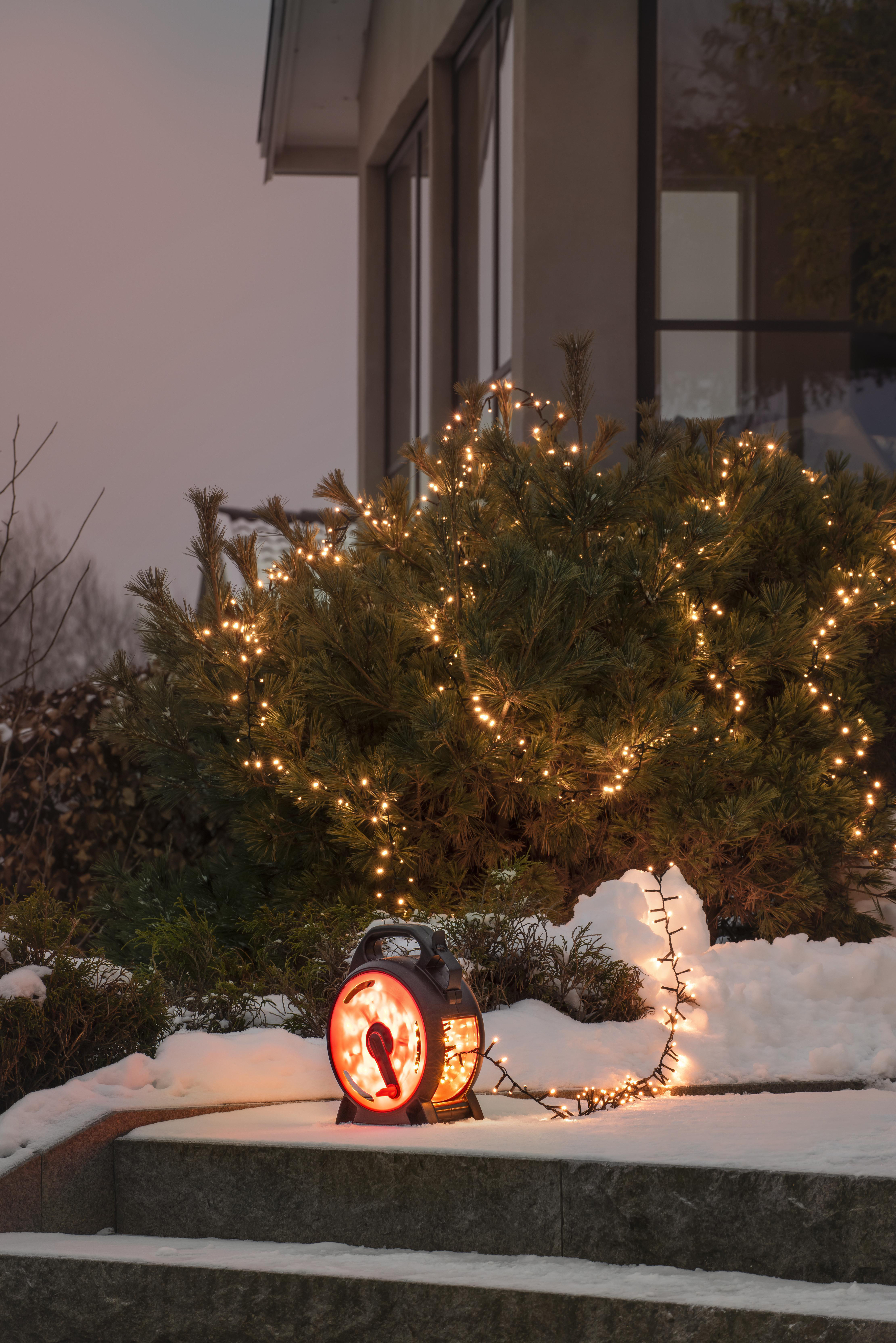 Außenszene in der Abenddämmerung. Beleuchtete Weihnachtslichter an einem Busch. Ein Heizgerät steht auf den Stufen.