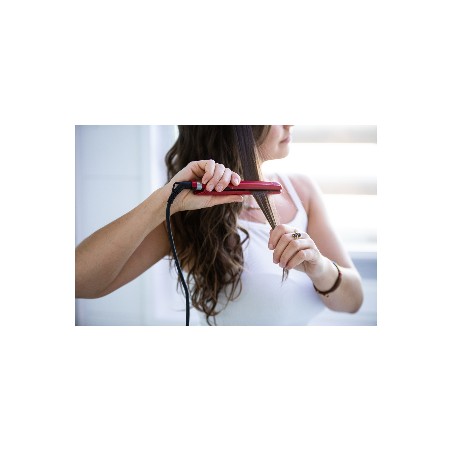 Una mujer alisándose el cabello con una plancha roja en un baño.