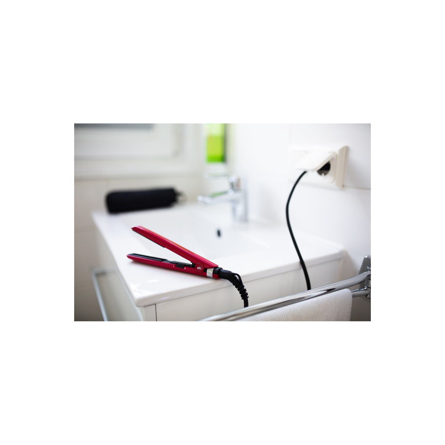 Plancha de pelo roja enchufada en un lavabo blanco, en un baño.