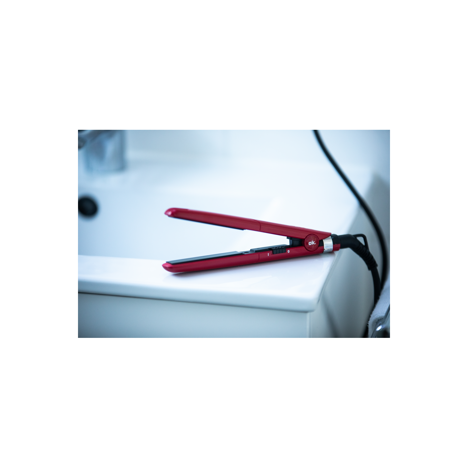 Plancha de pelo roja sobre un lavabo blanco. El cable está enchufado en el lado derecho.