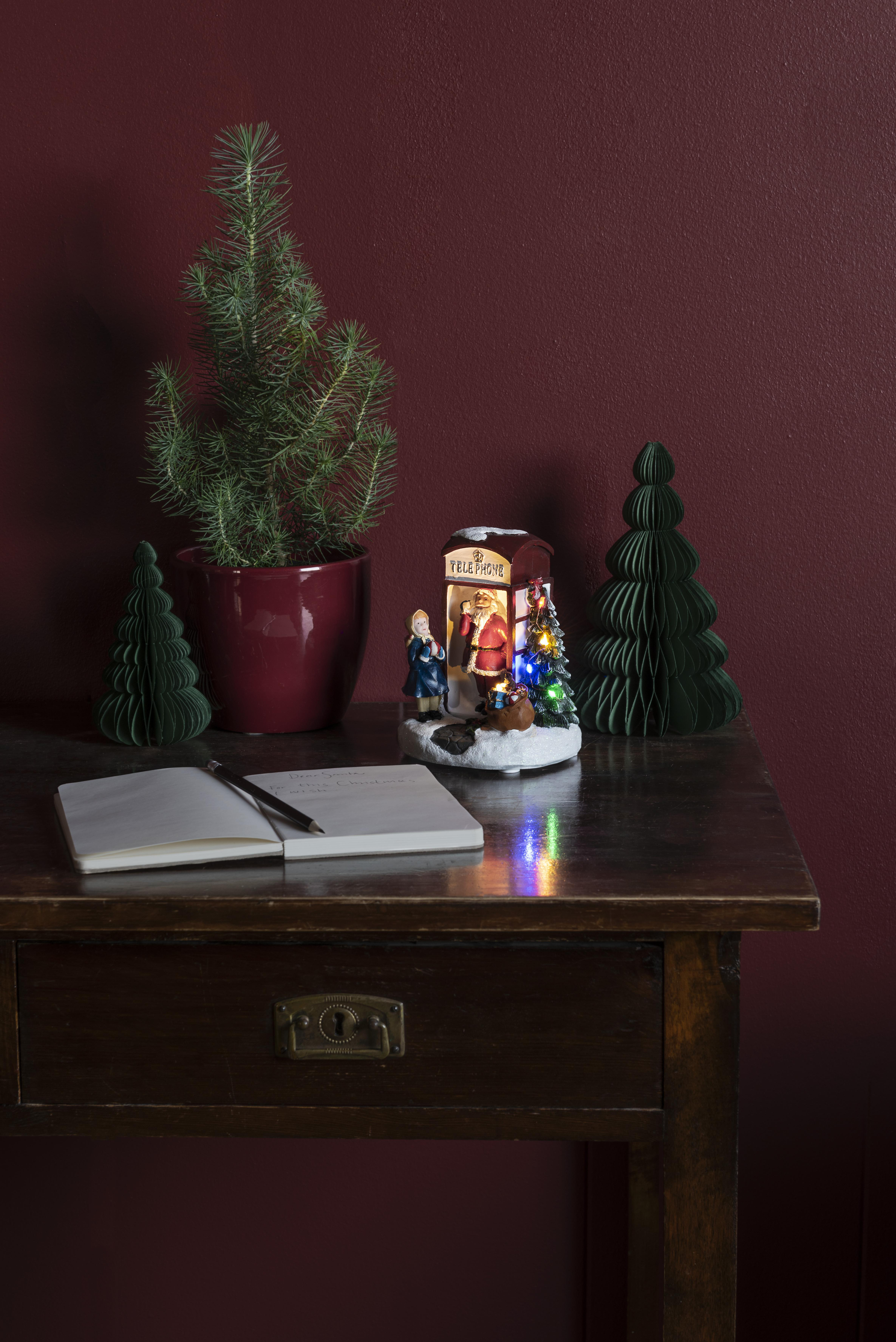 Weihnachtsszene mit kleinem Baum, Santa-Ornament, Notizblock und Stift auf Tisch.