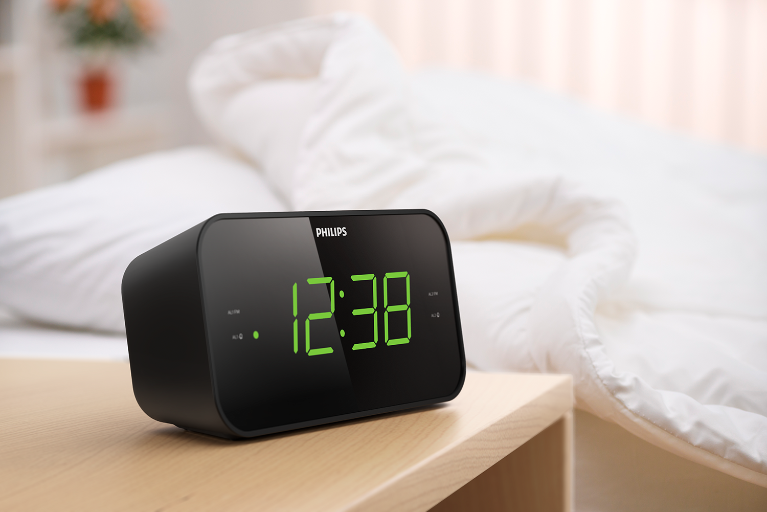 Black Philips alarm clock displaying 12:38. The clock sits on a wooden table beside a bed.