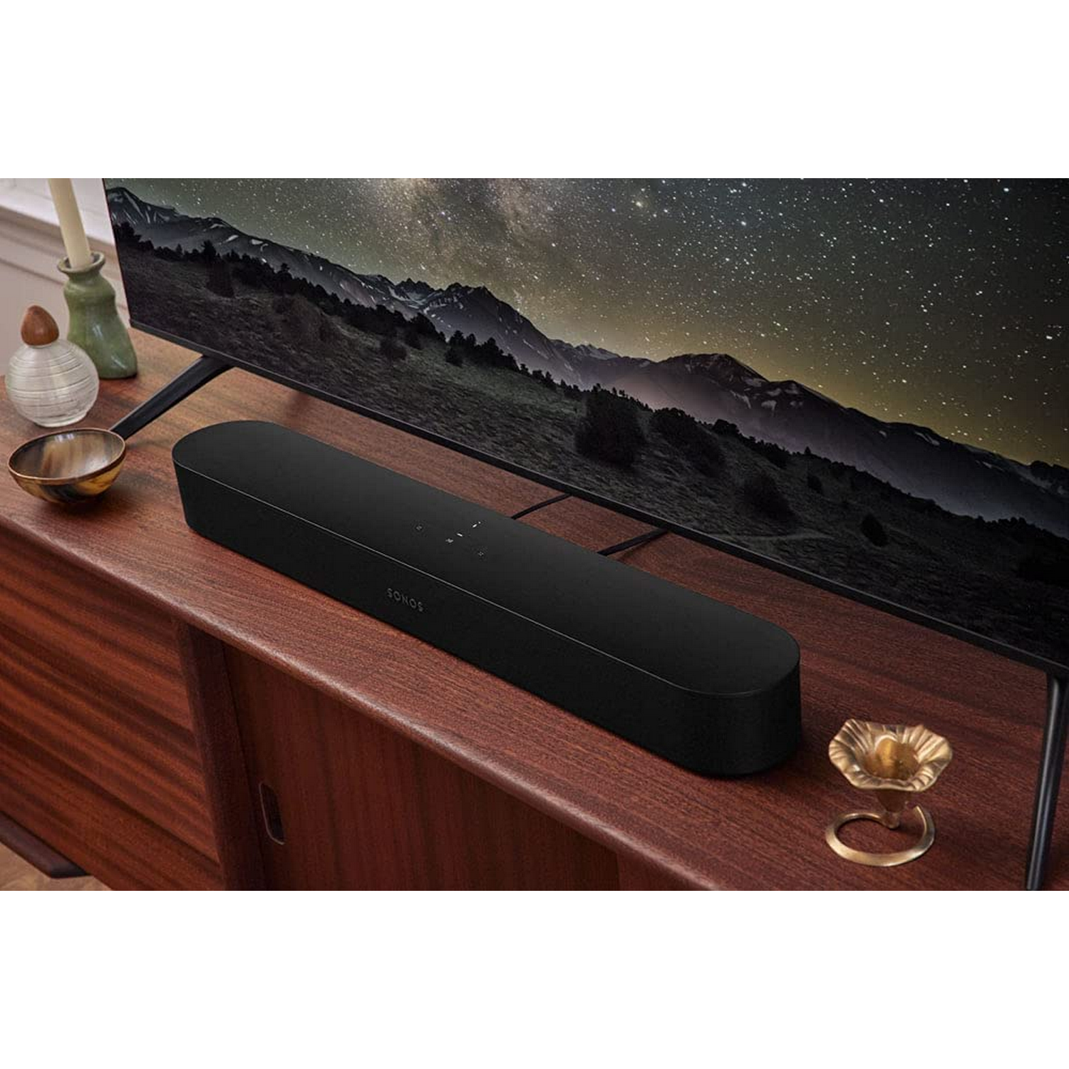 Una barra de sonido negra sobre un mueble de madera. Un televisor está encima, mostrando un cielo nocturno estrellado.