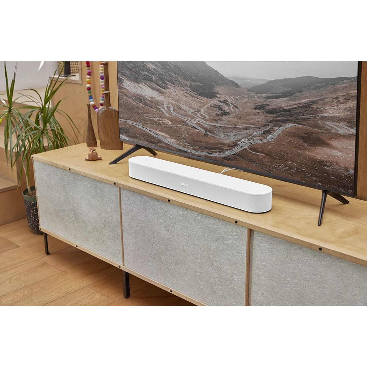 Barra de sonido blanca sobre mueble de madera. TV montada en la pared. Fondo borroso.