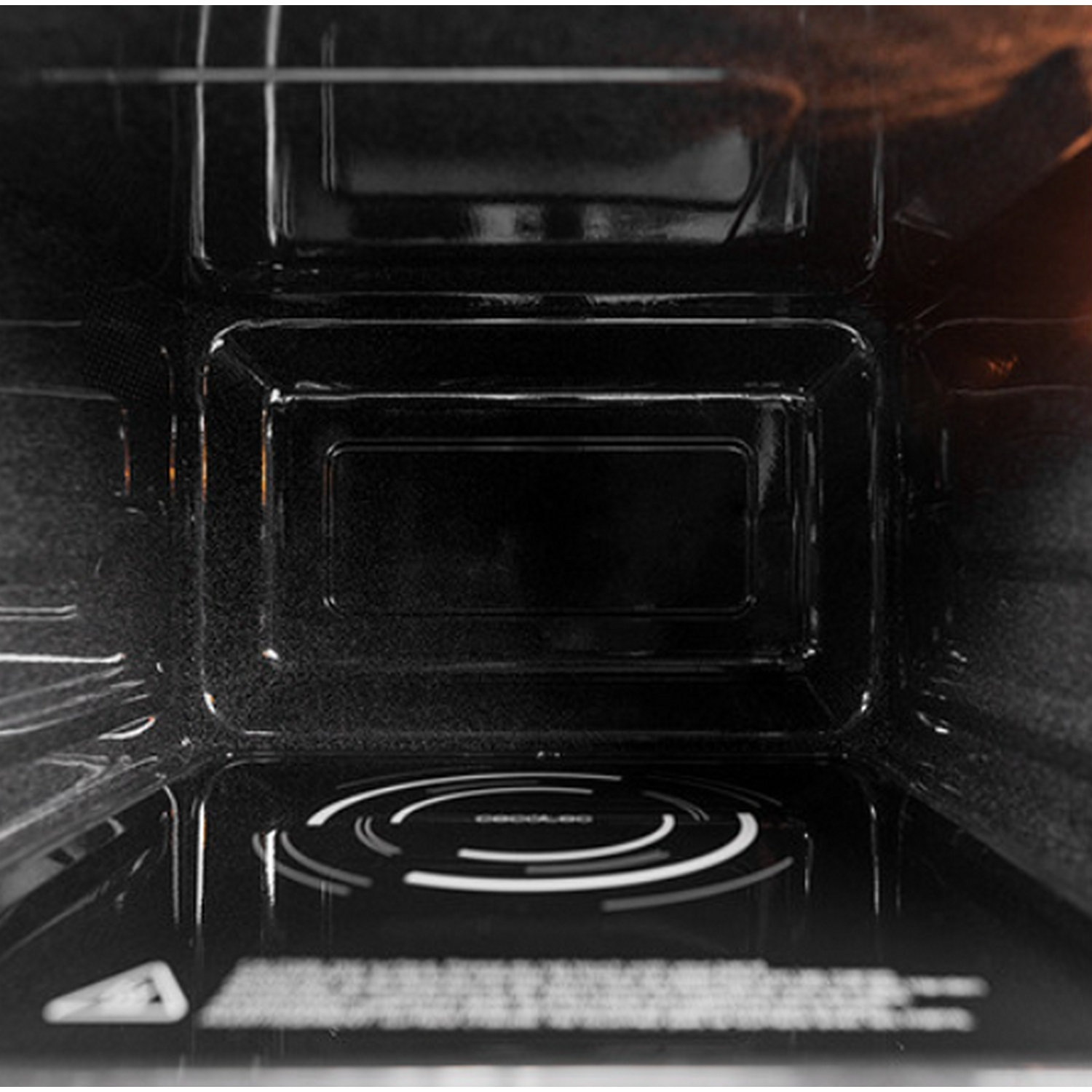 El interior de un microondas negro. La superficie es reflectante y hay un patrón.