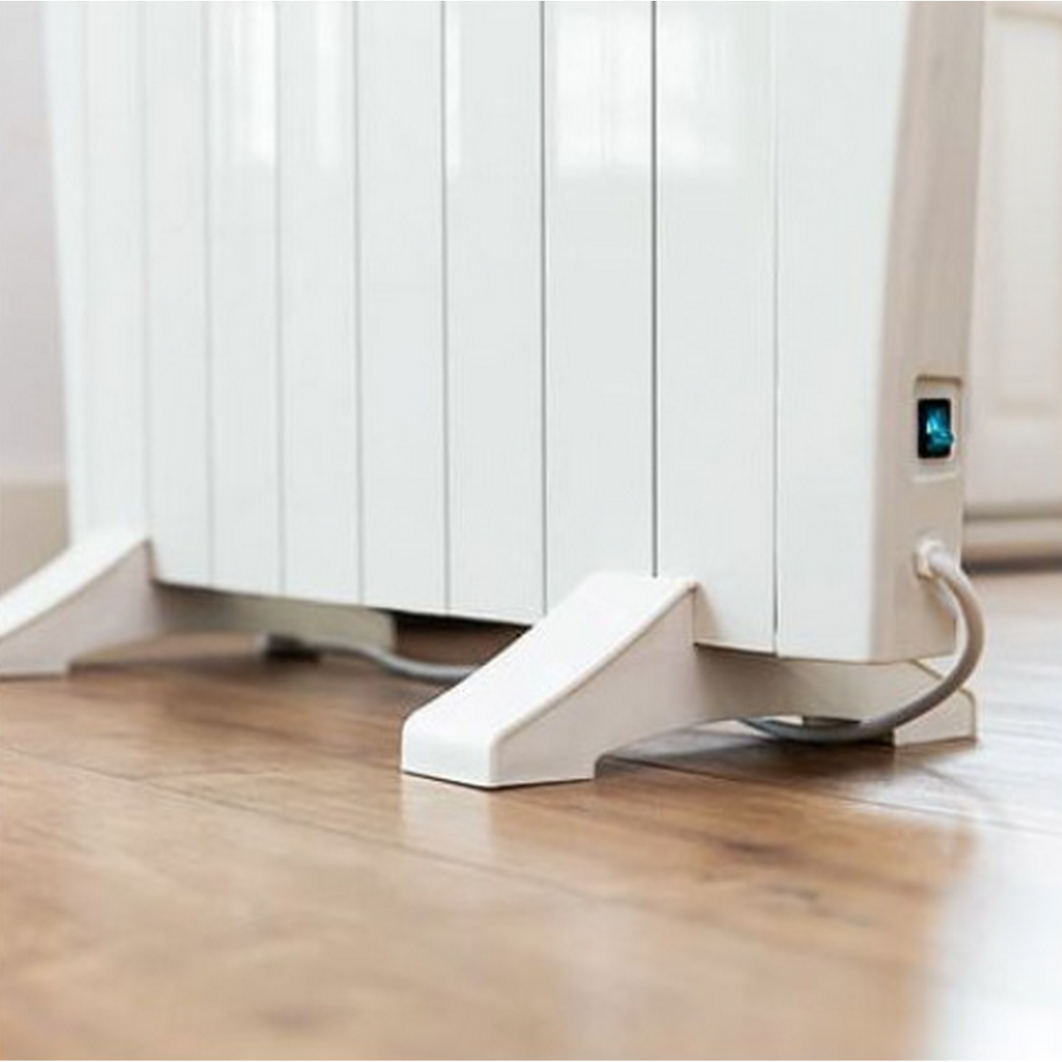 Un calefactor eléctrico blanco. Está en un suelo de madera. El lado tiene un botón de encendido.