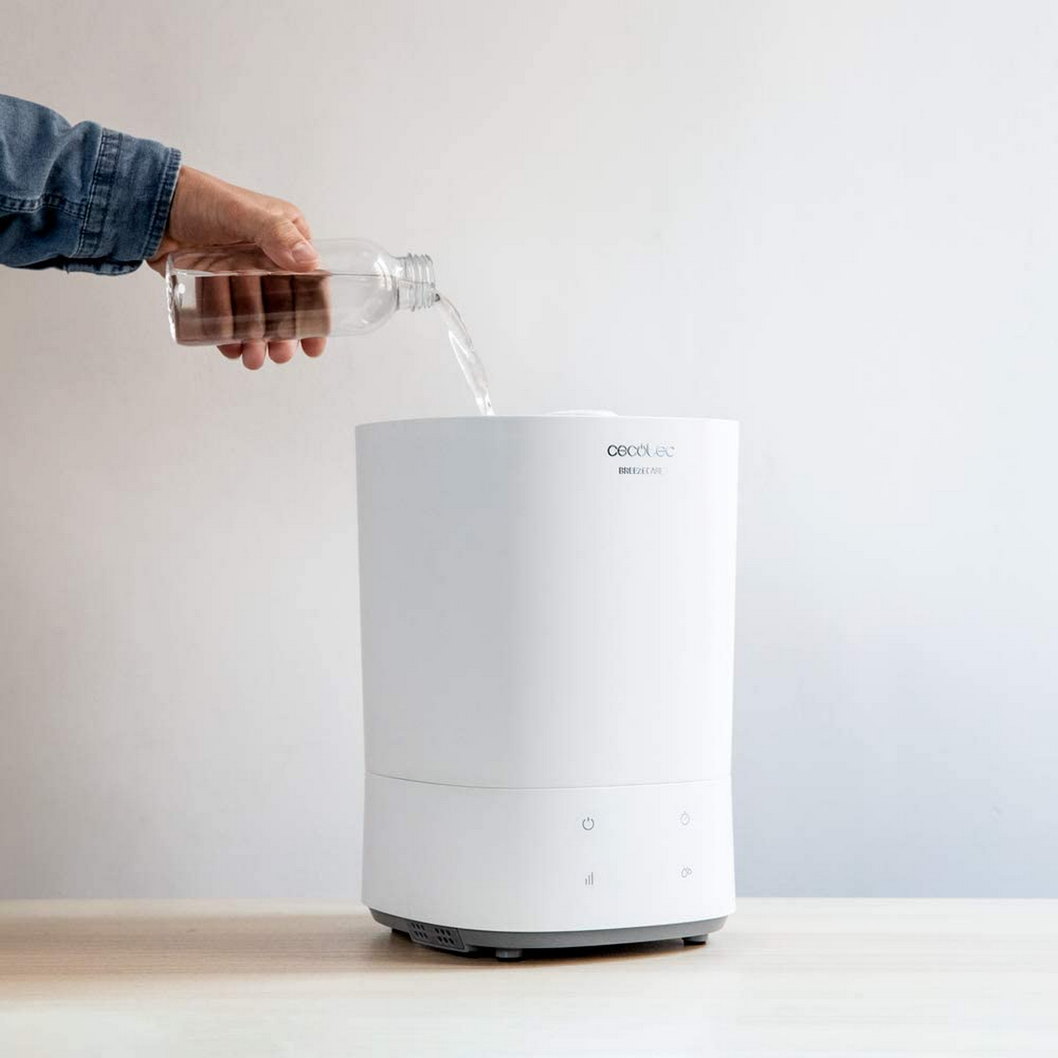 Una mano vierte agua de una botella en un humidificador blanco sobre una mesa.